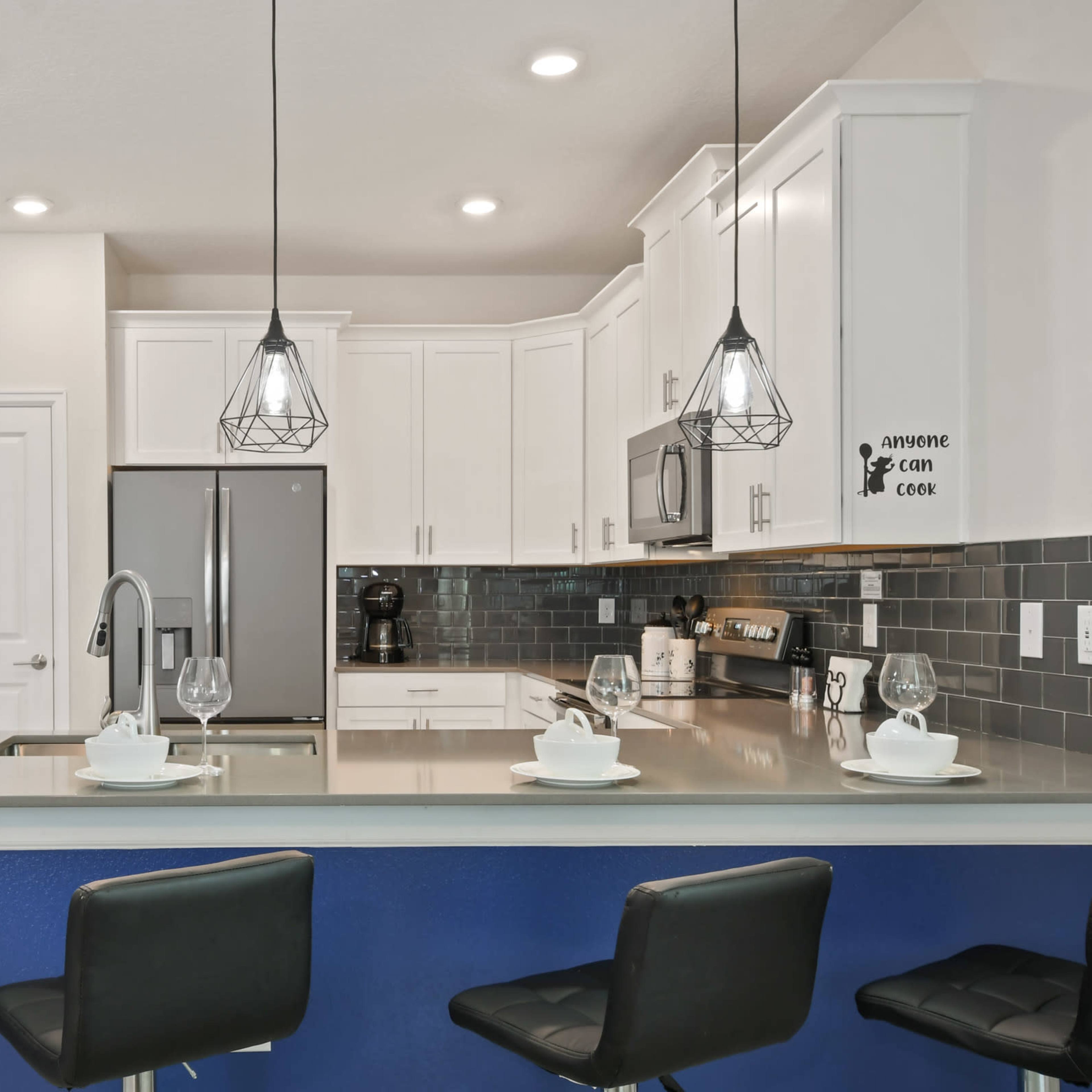 A modern kitchen with white cabinets, stainless steel appliances, and four black bar stools at a blue-topped island.