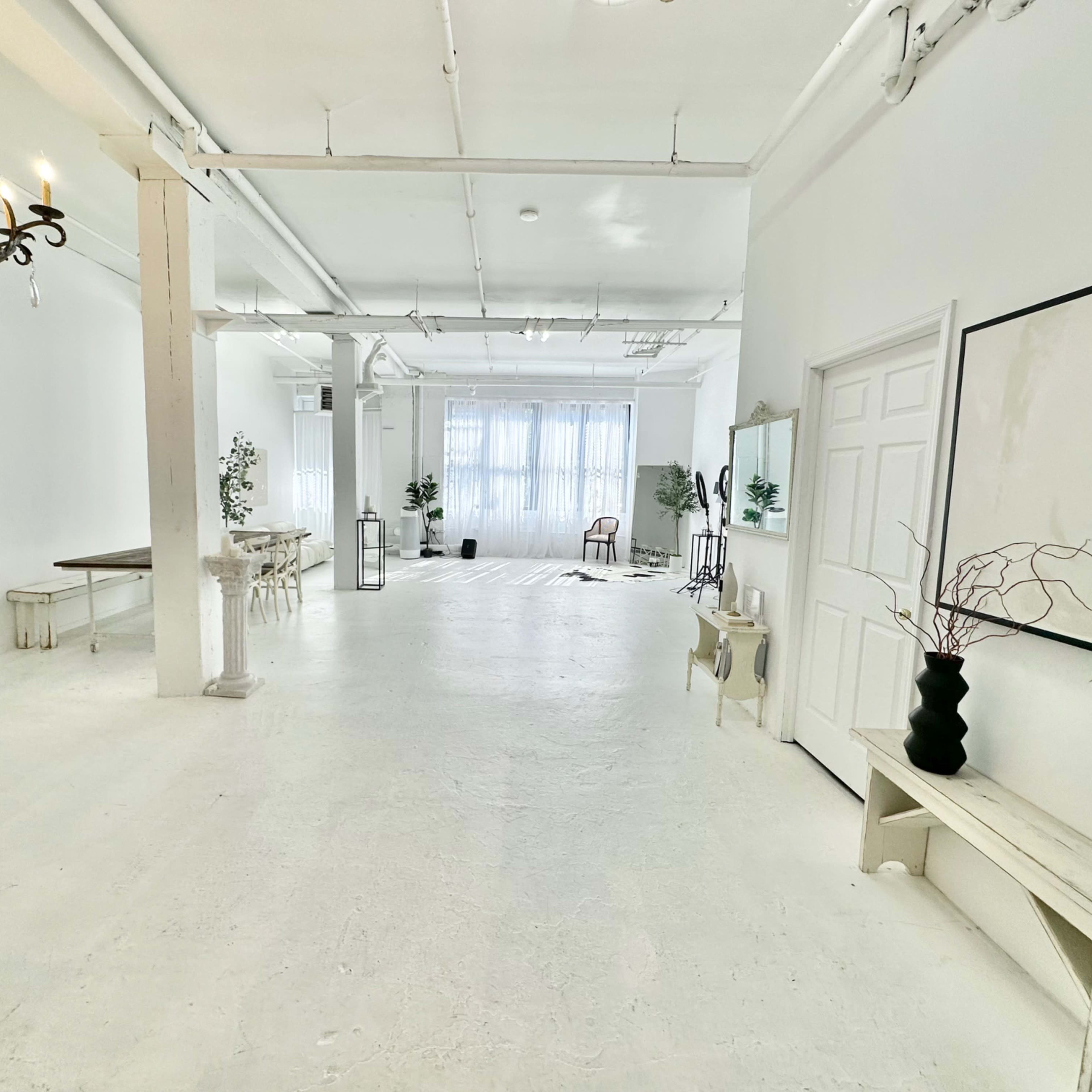 A bright, spacious, and empty room with white walls, wooden furniture, and large windows allowing natural light to enter.