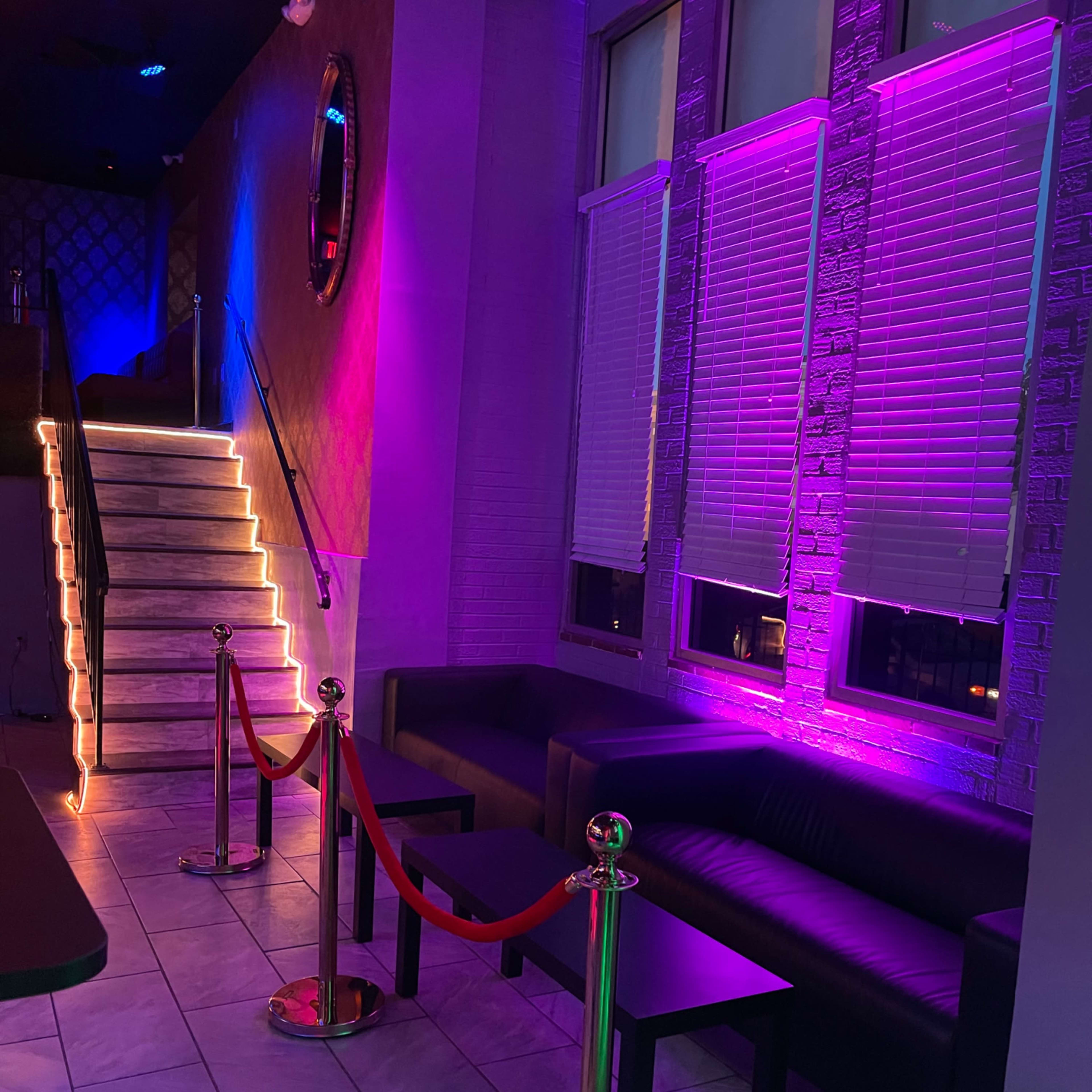 The interior features a staircase illuminated with LED lights, flanked by sectional couches and velvet rope barriers.