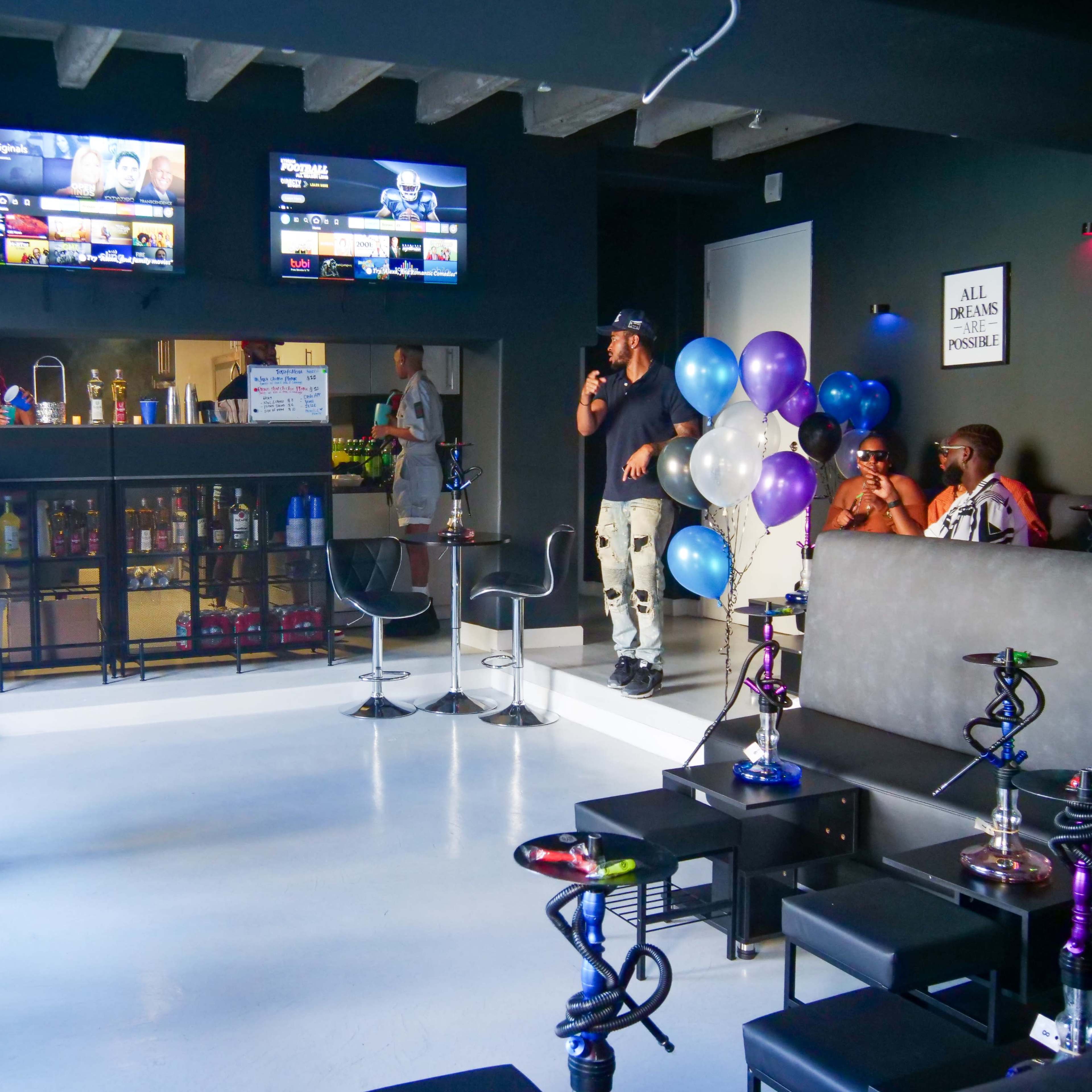 A modern lounge features multiple televisions, hookah setups, and patrons seated at tables, surrounded by balloons and a snack bar.
