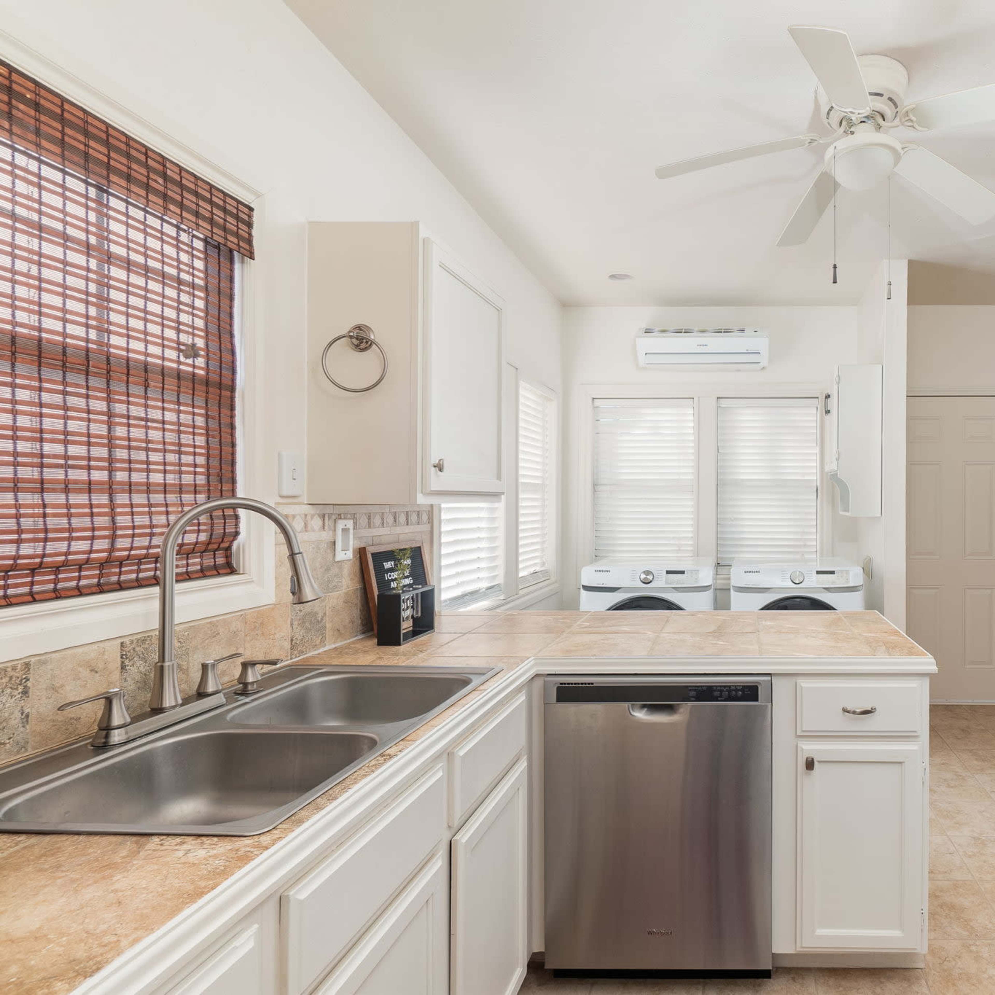 A kitchen with white cabinets, a stainless steel sink, a red refrigerator, and washer and dryer units in a bright, open layout.