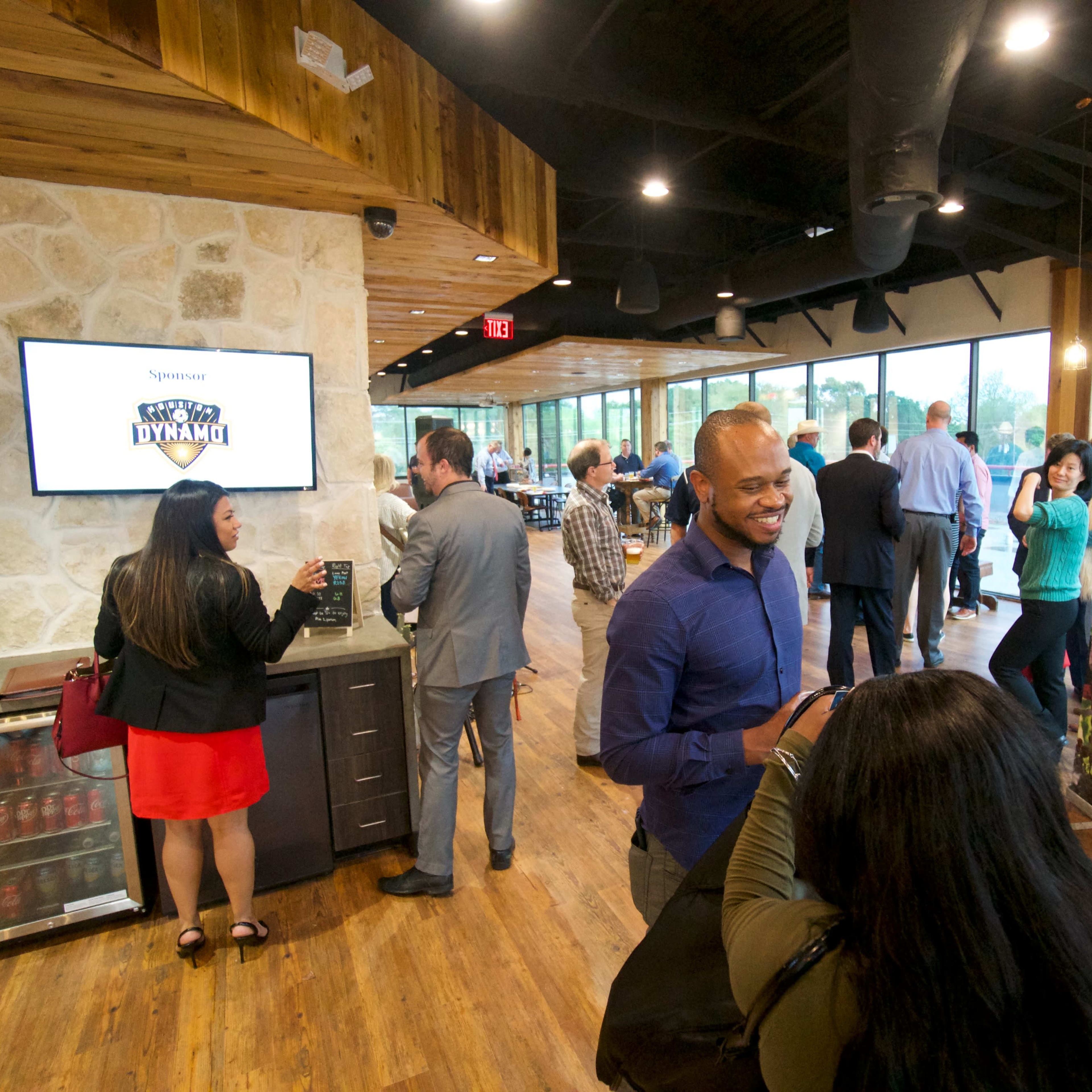A group of people mingles at a networking event inside a modern venue with wood and stone decor and large windows.