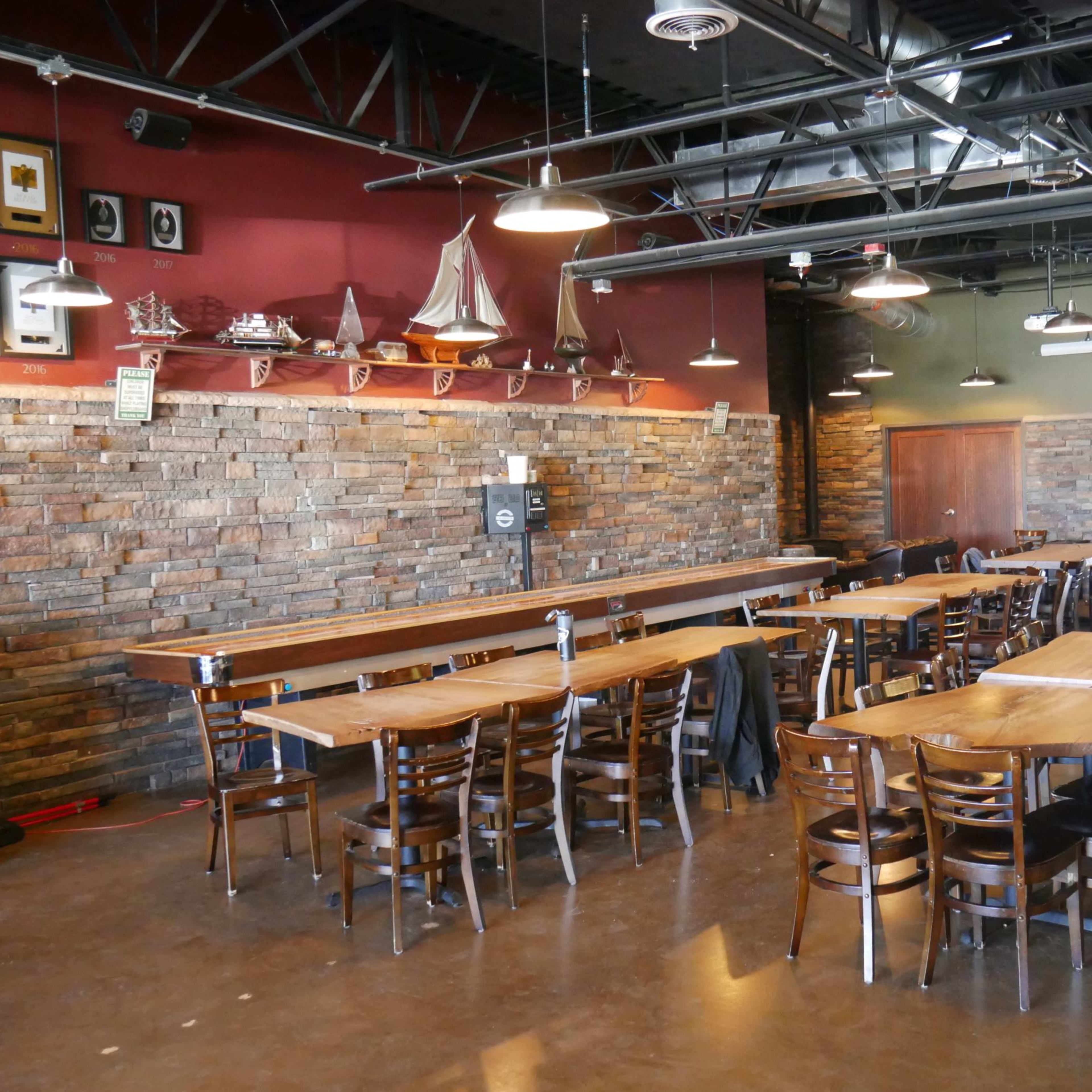 A spacious restaurant interior with wooden tables and chairs arranged in rows, and a stone wall adorned with decorative items.