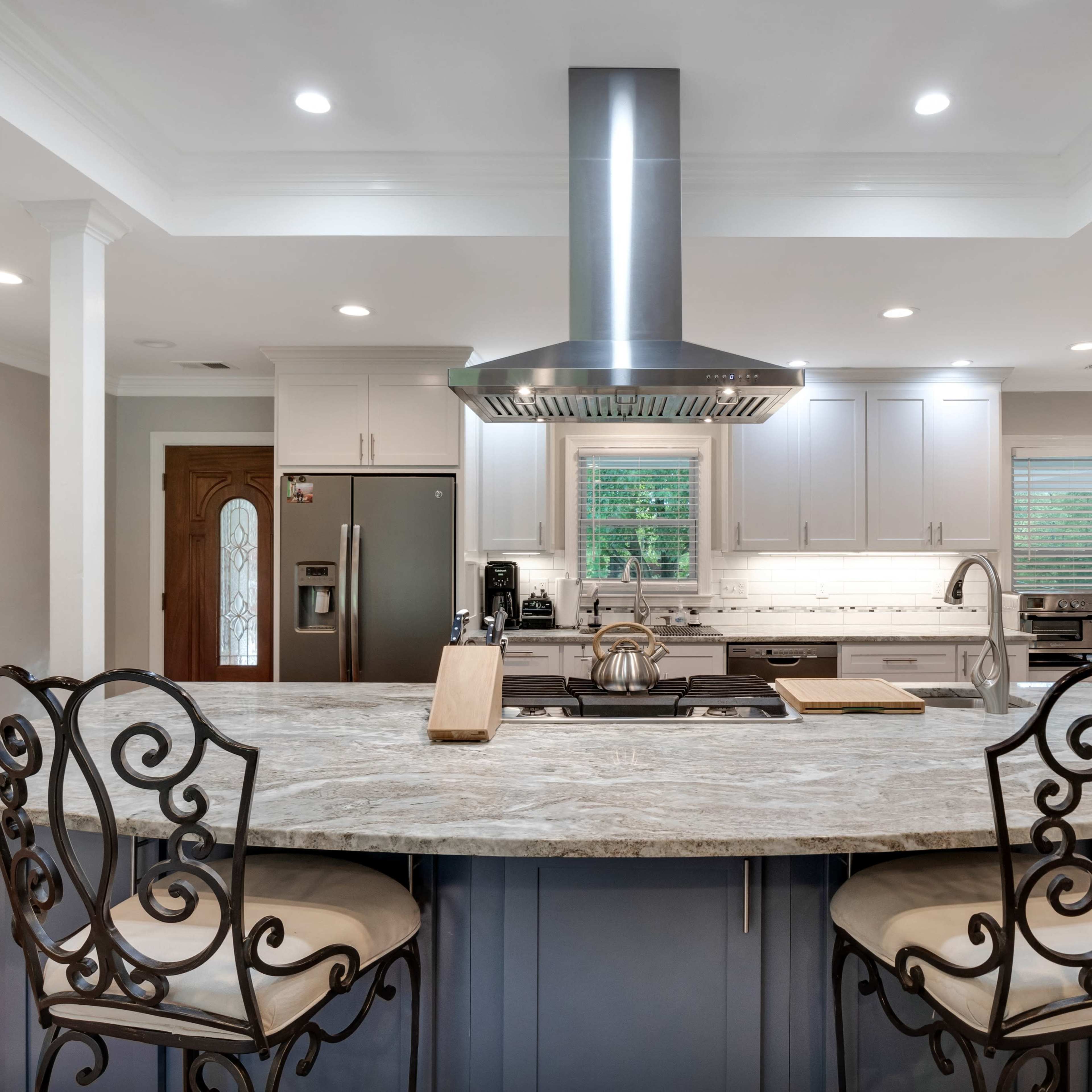 A modern kitchen features a central island with bar seating, stainless steel appliances, and a range hood above the cooktop.