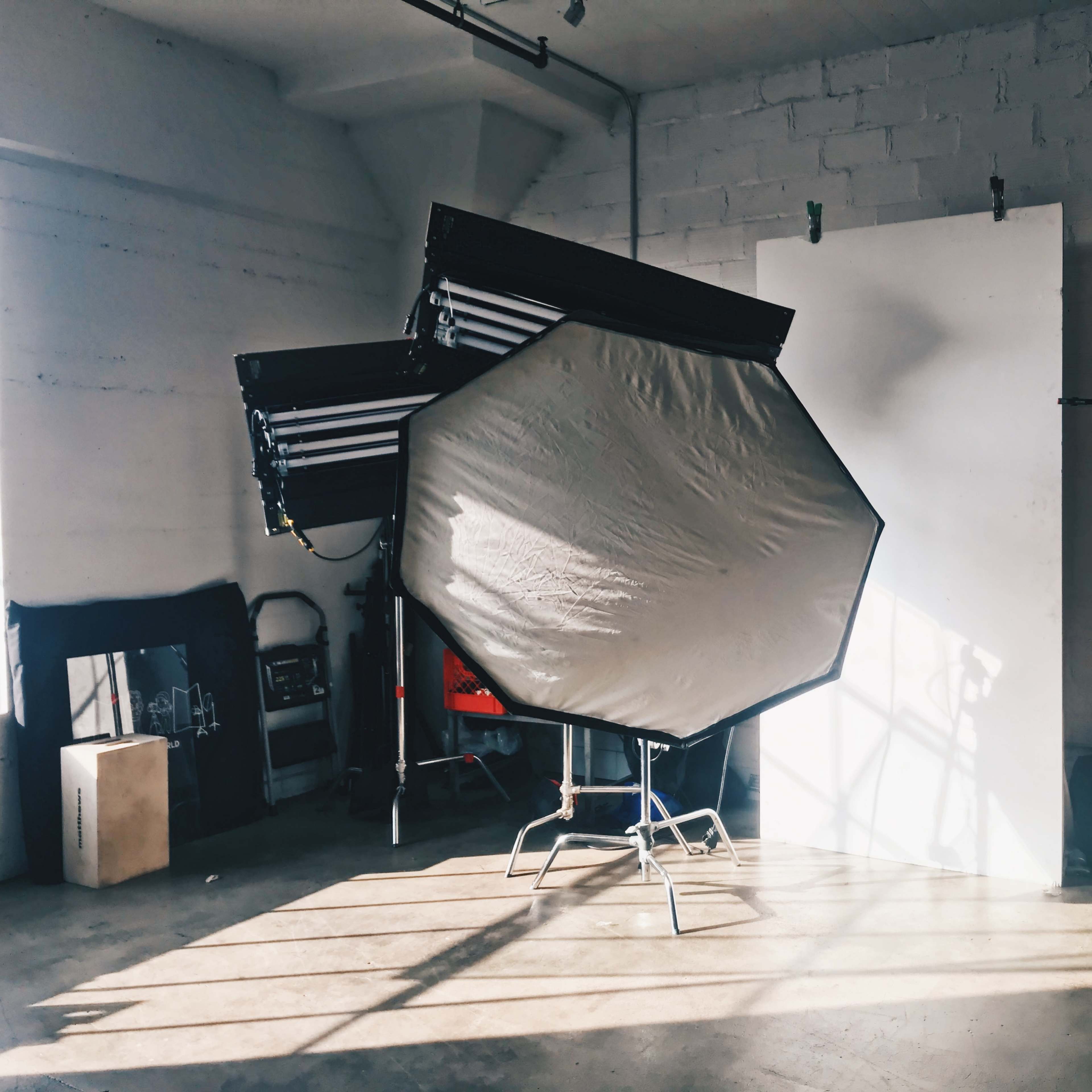 A large octagonal softbox is positioned in a well-lit photography studio with a white backdrop and a storage unit.