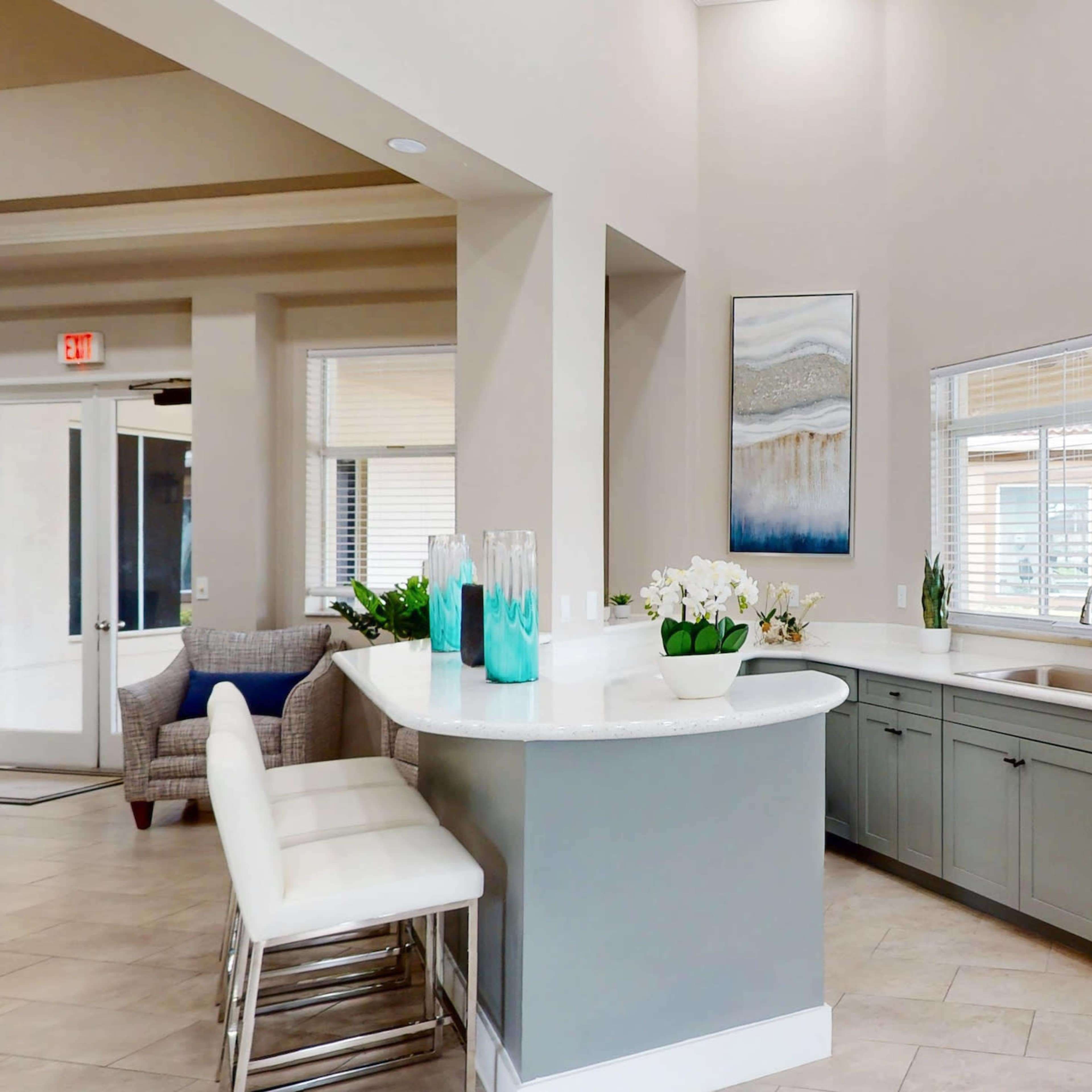 A modern kitchen with a gray island, white countertop, and large windows allowing natural light to fill the space.