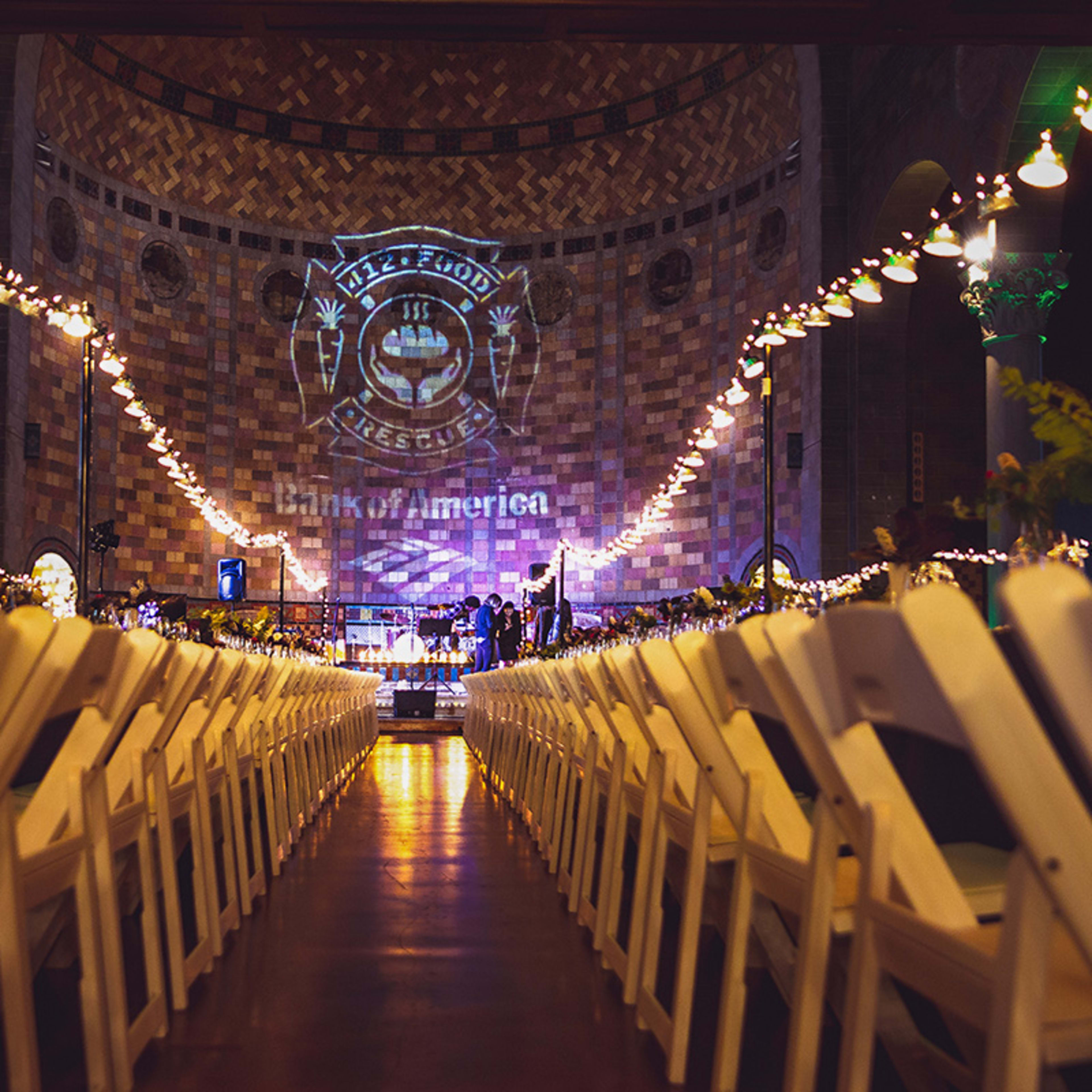 An interior event space features rows of white chairs set up for a gathering, with a large projection on the wall displaying a logo and the words "Bank of America."