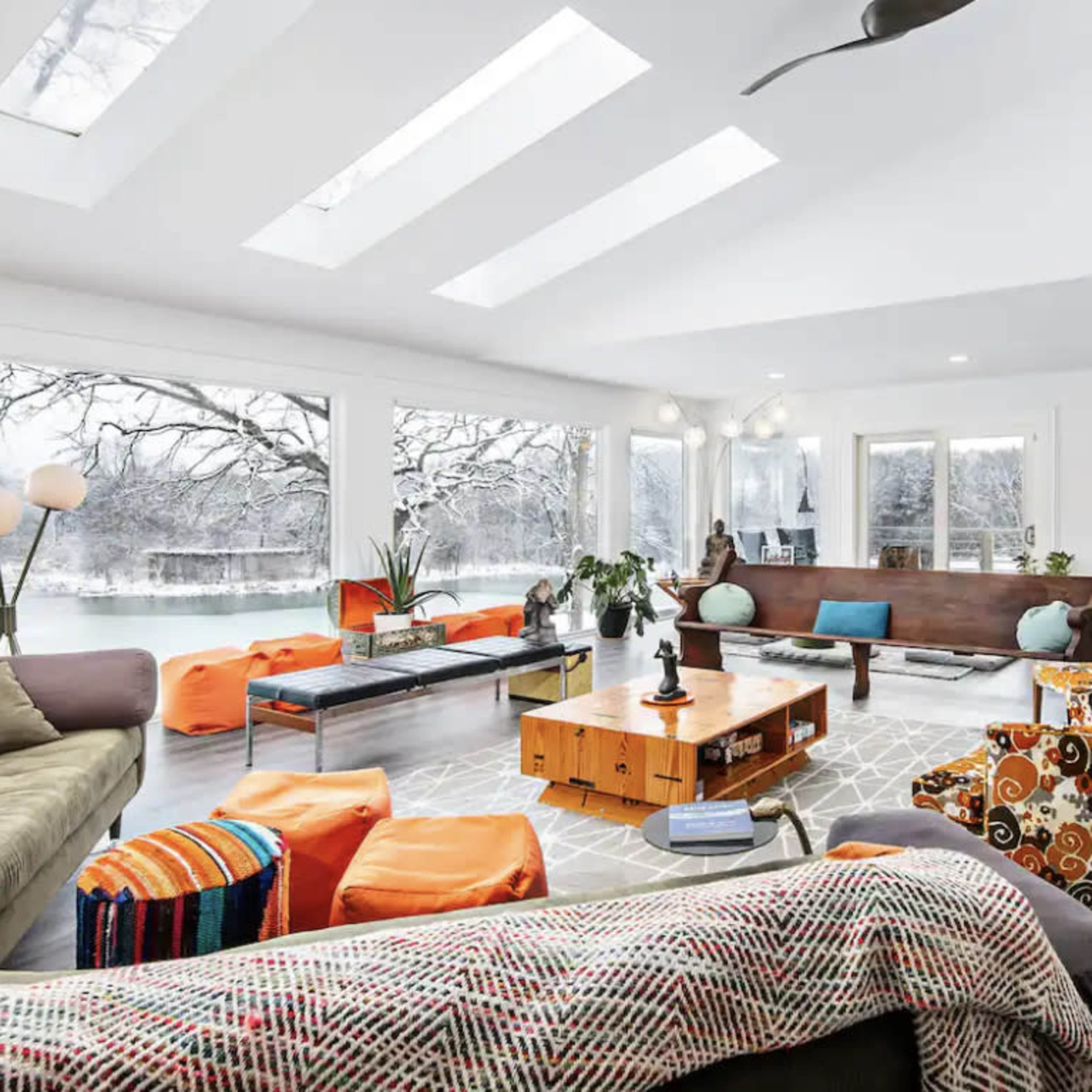The spacious living room features large windows overlooking a snowy landscape, with comfortable seating, a coffee table, and a dining area.