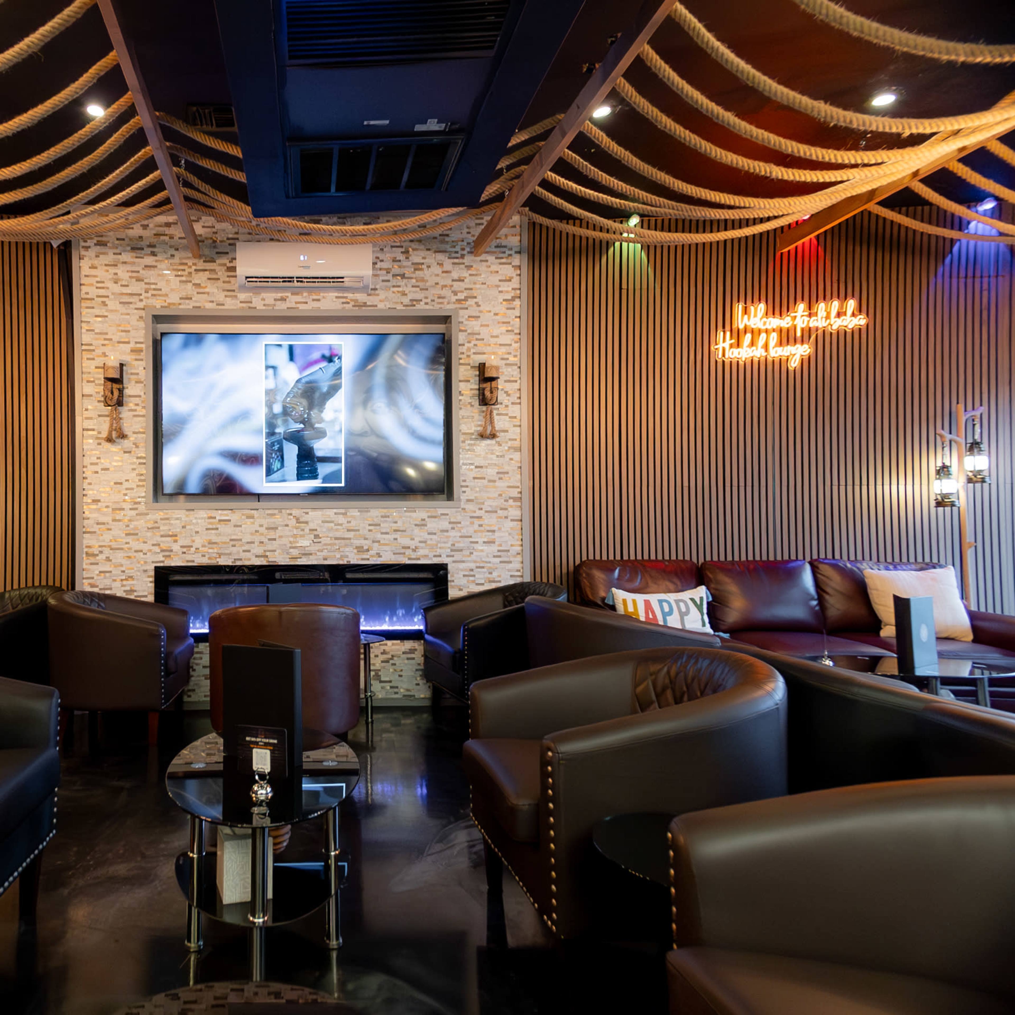 A lounge area with dark leather seating, a large wall-mounted screen, and decorative lighting along the ceiling.