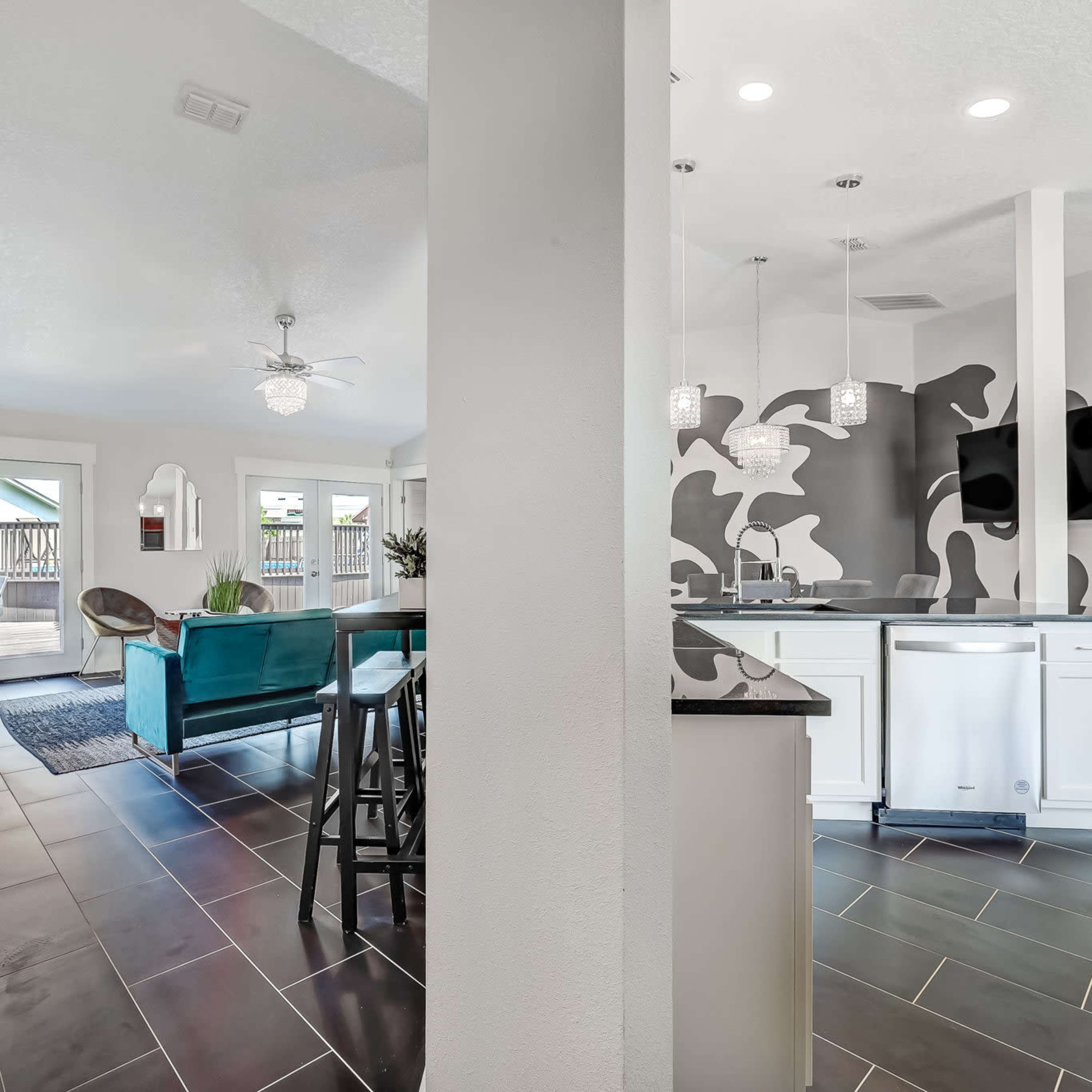An open-concept living area with a kitchen featuring a modern design, contrasting black and white walls, and seating areas leading to an outdoor patio.