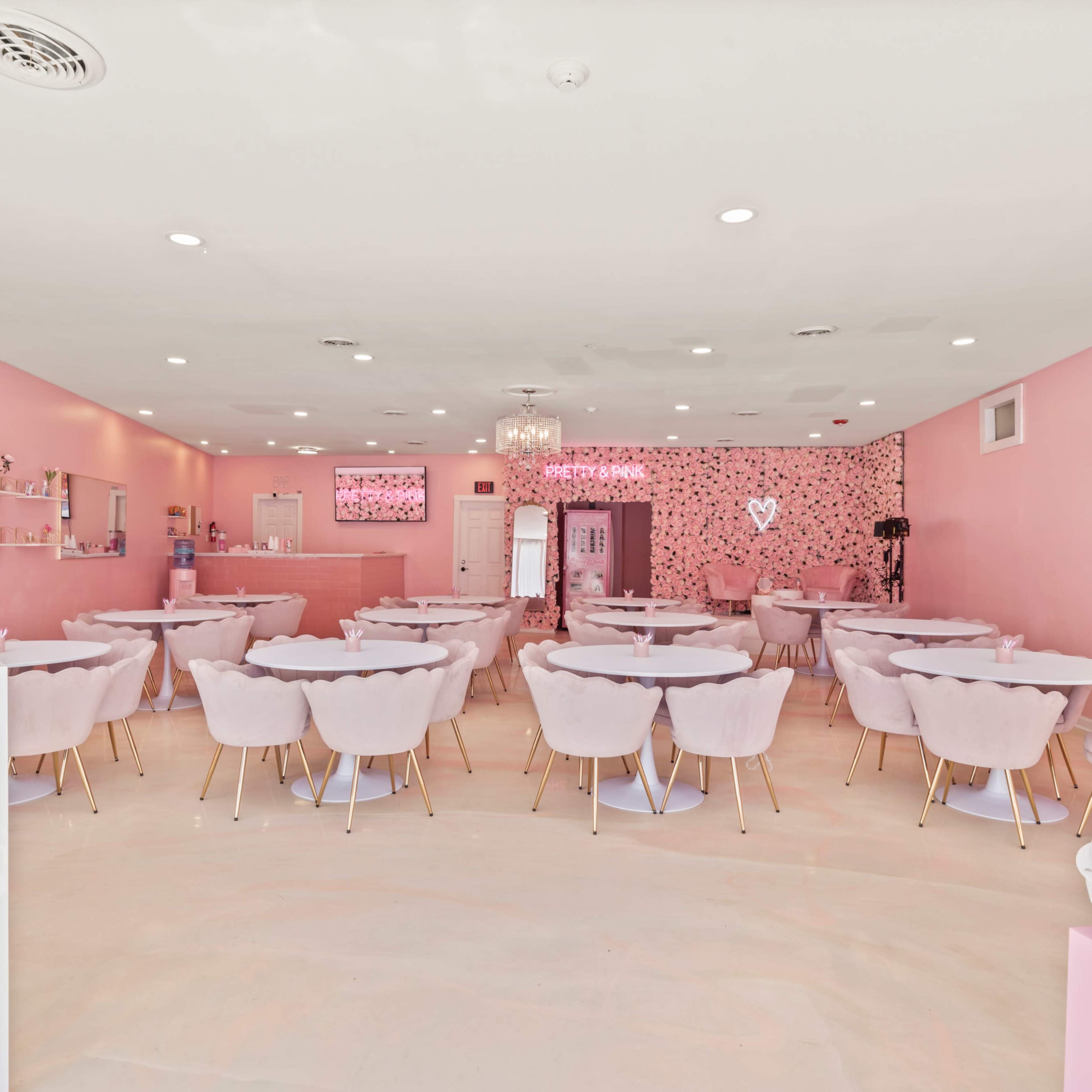 A pink-themed café with round tables and chairs, floral wall decor, and a bar area at the back.