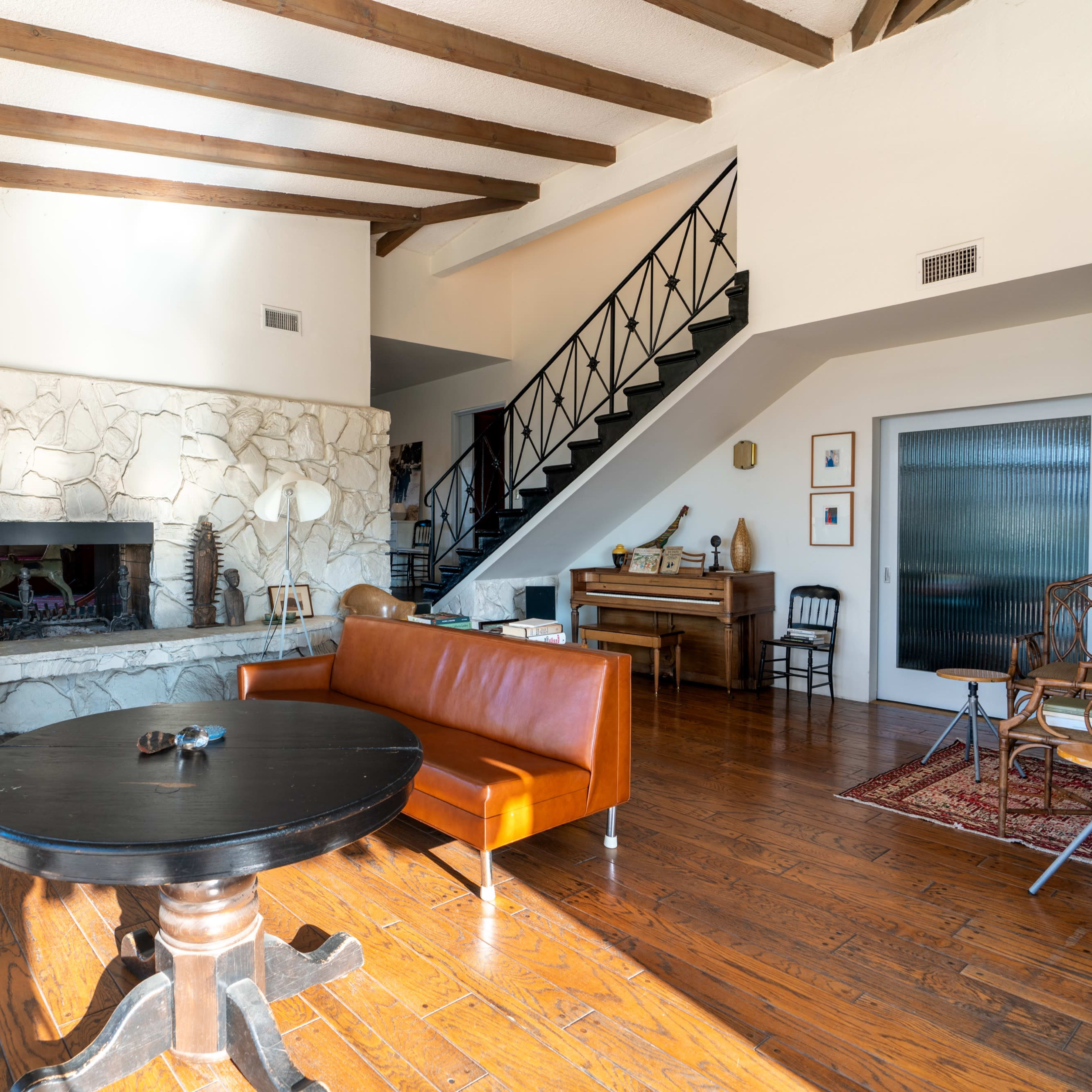 A spacious living room with a stone fireplace, wooden beams on the ceiling, and a mix of modern and rustic furniture.