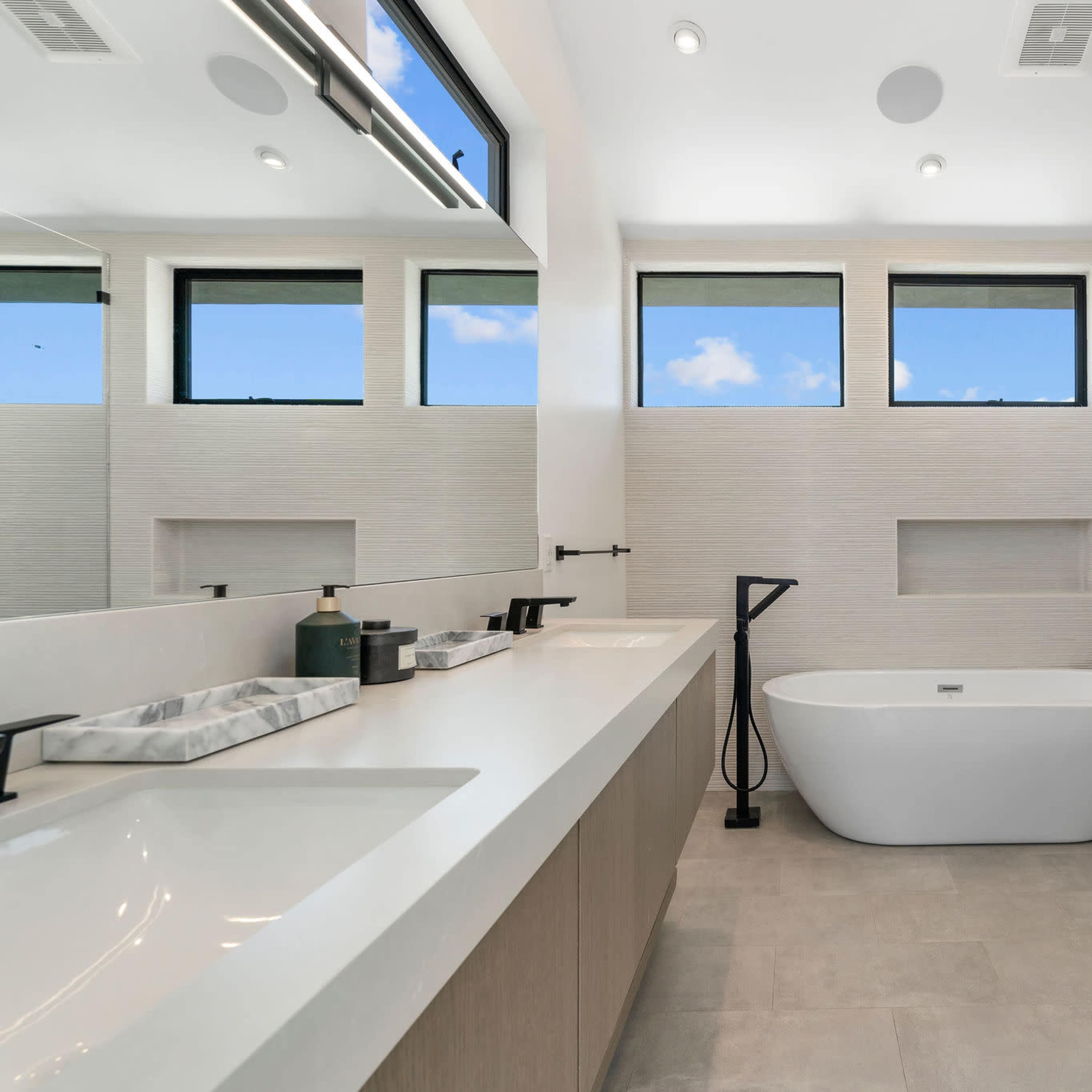 A modern bathroom with a freestanding bathtub, dual sinks, large mirrors, and glass walls reflecting natural light.