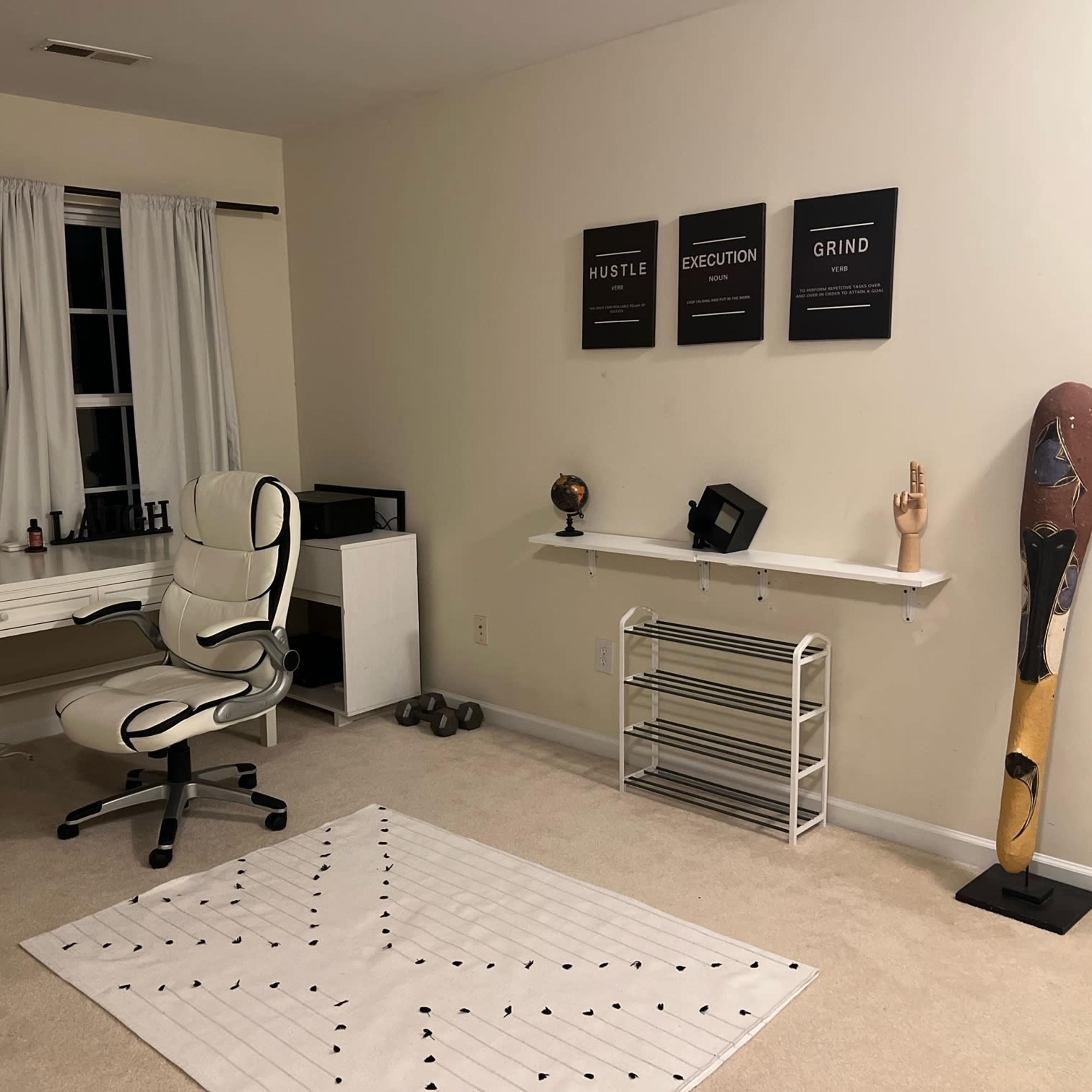 The room features a desk with a white chair, shelving with decor, exercise weights on the floor, and a large, decorative totem against the wall.