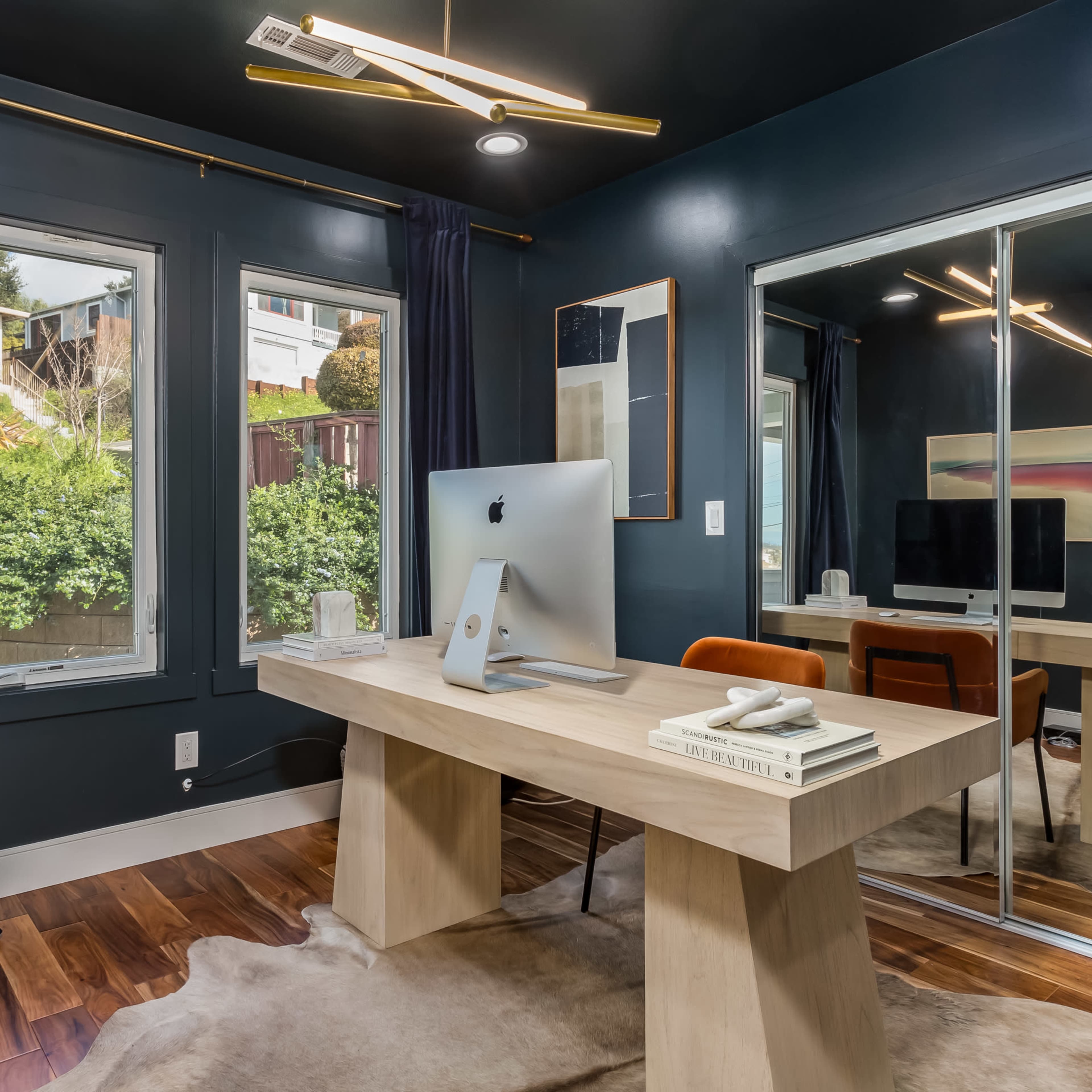 A modern home office with a wooden desk, an iMac, and large windows framed by dark curtains.