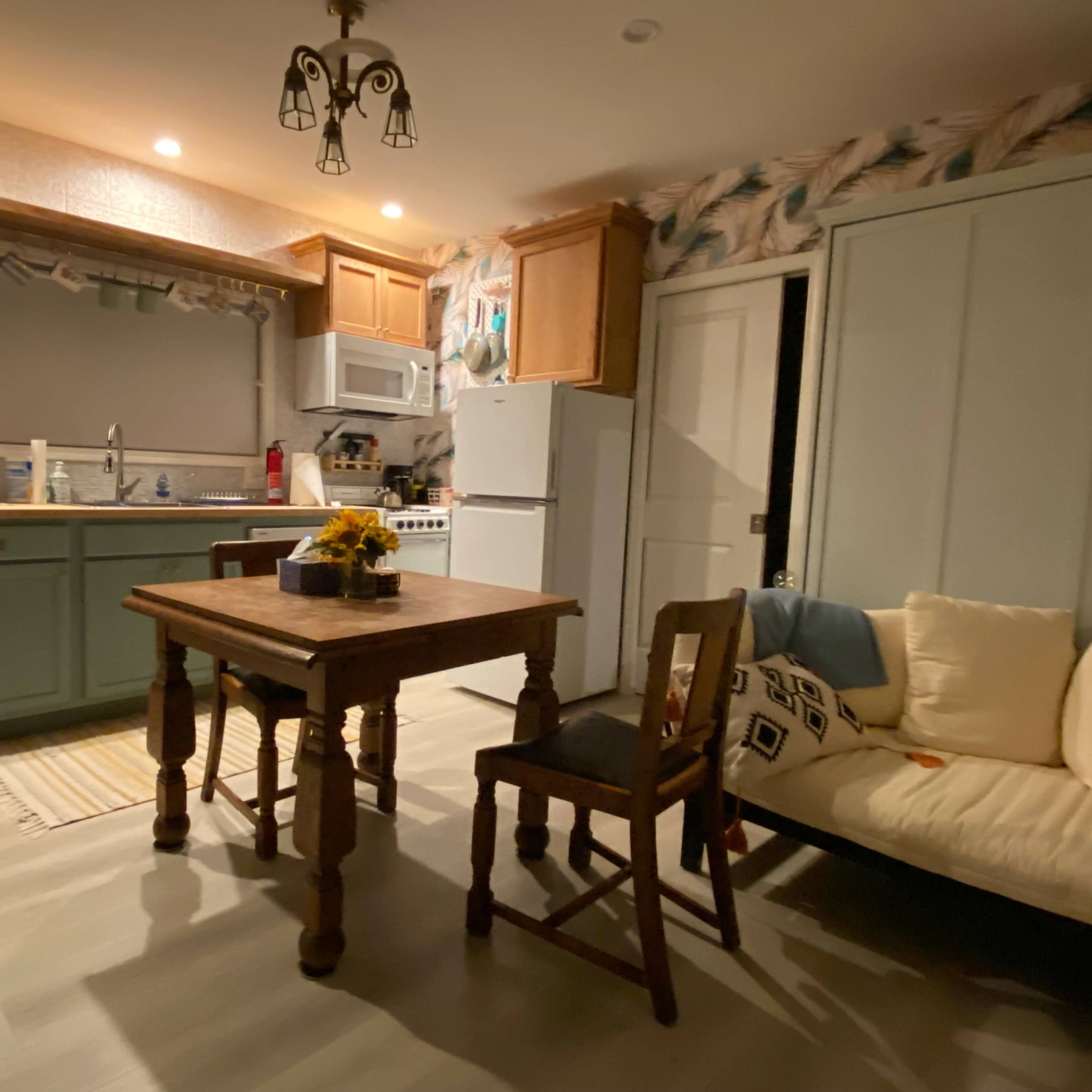 A small kitchen area features a wooden table with two chairs, a sink, and appliances, along with a couch along the wall.