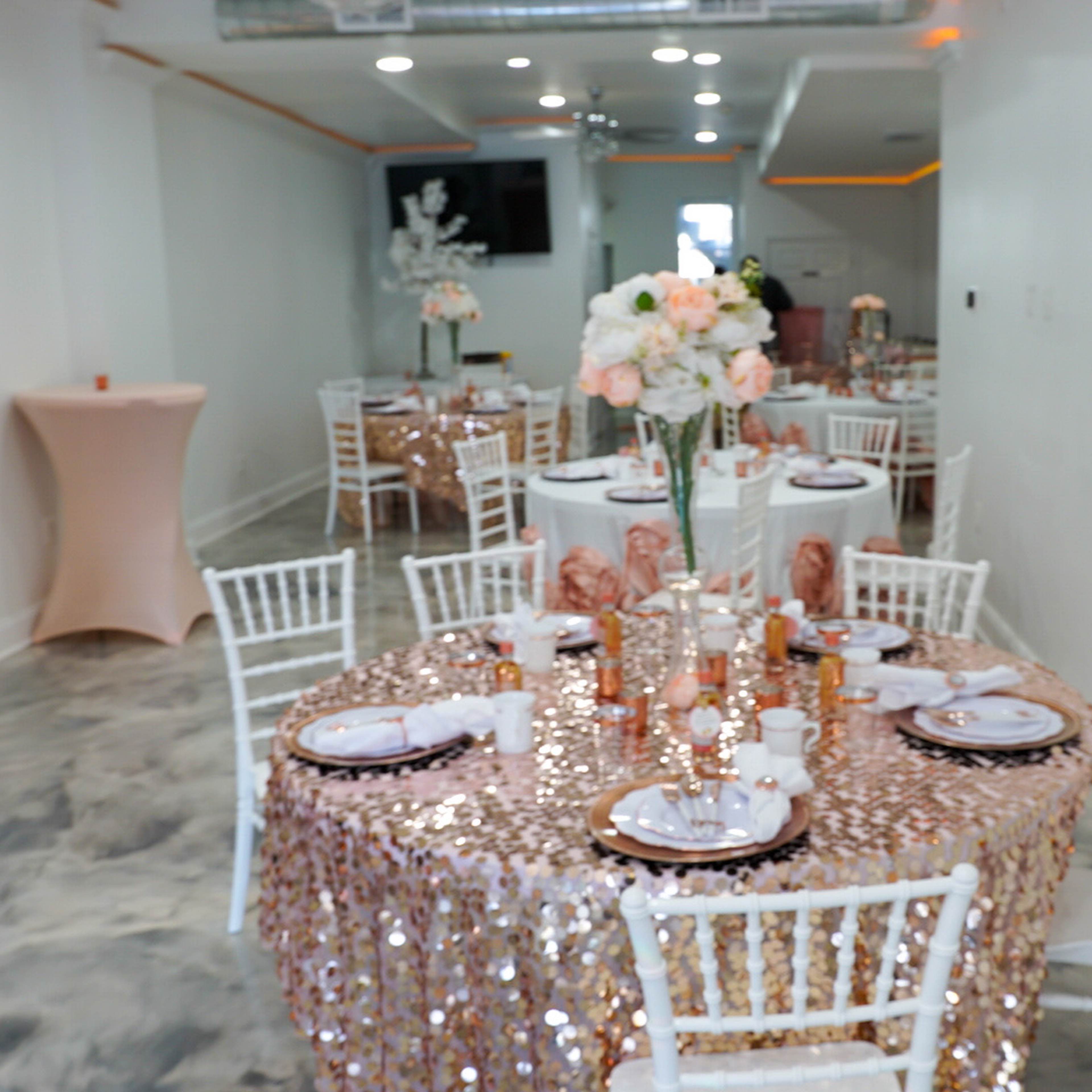 A banquet hall decorated with sequined tablecloths, elegantly set tables, and floral centerpieces.