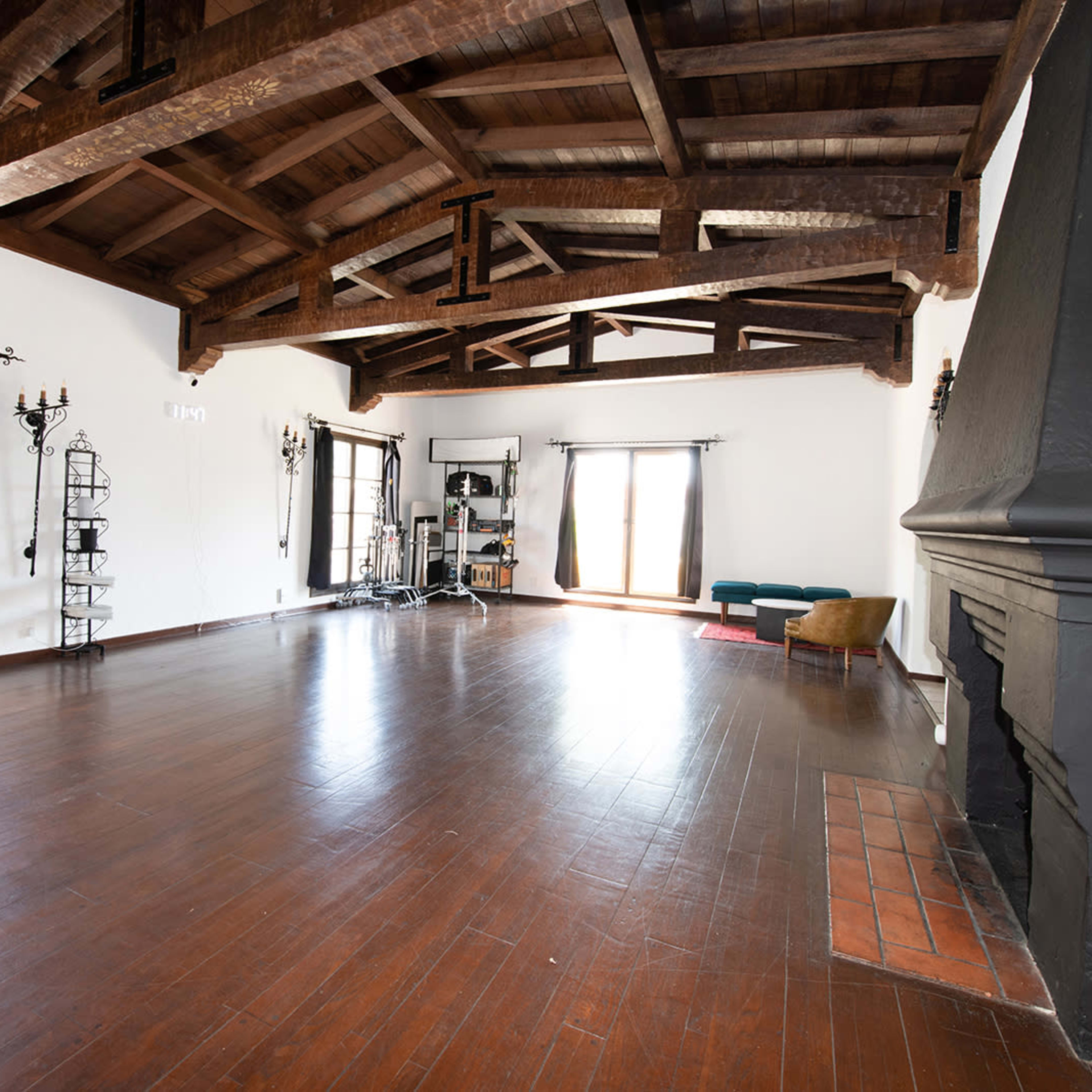 A spacious room with wooden beams, large windows, and a fireplace, featuring minimal furniture and an open layout.