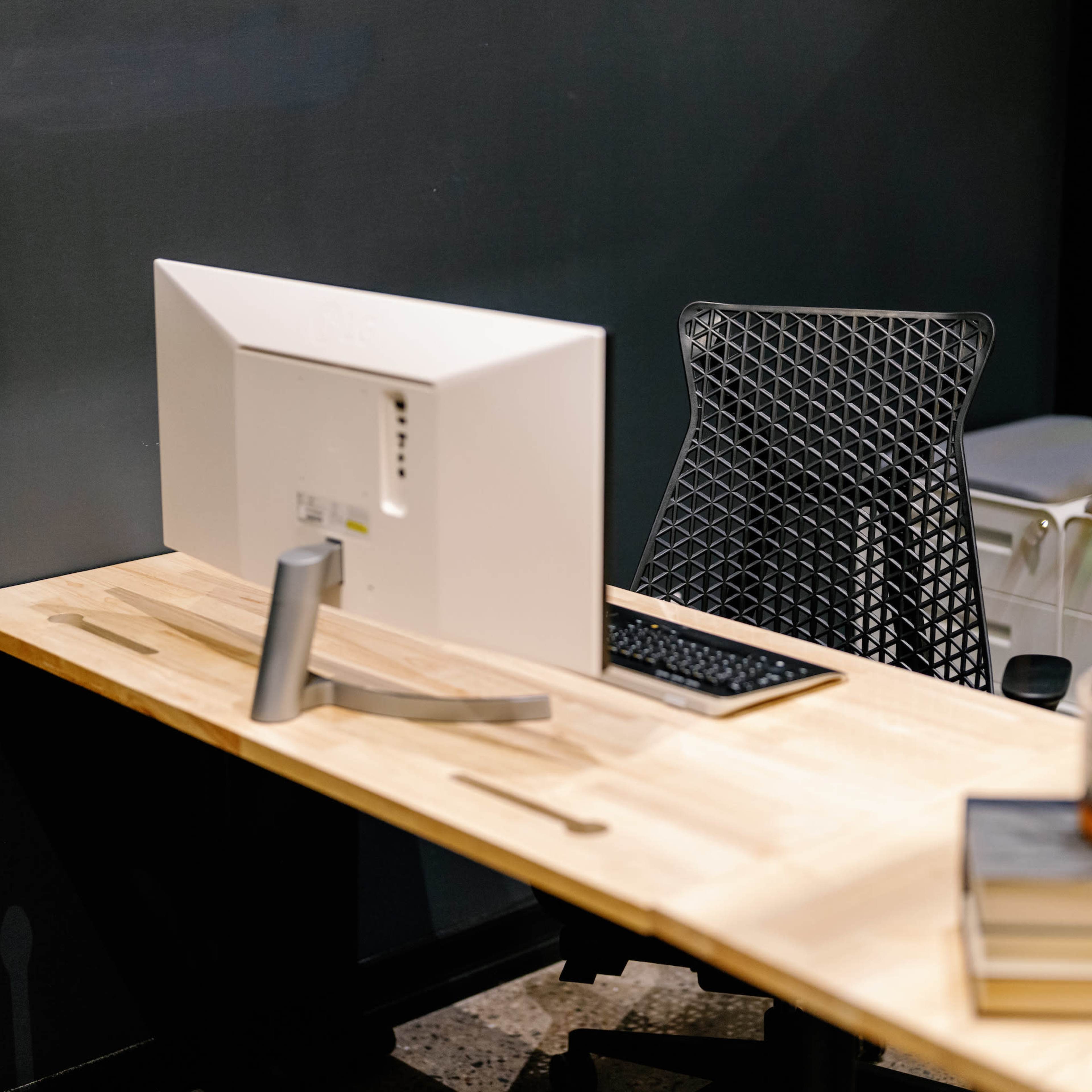 A modern desk with a computer monitor and keyboard, accompanied by a small potted plant and stacked books.