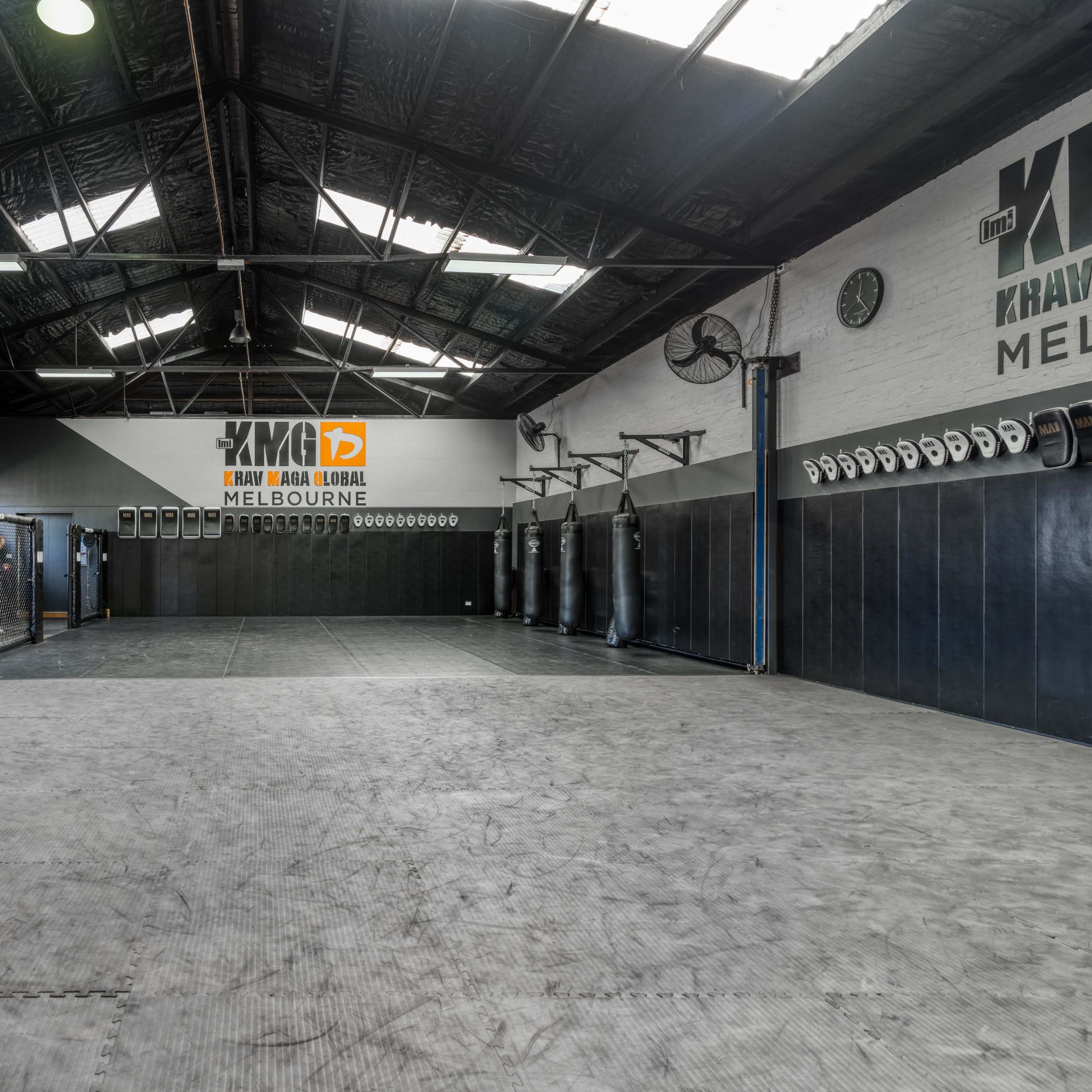 An empty martial arts training facility with punching bags and fitness equipment along the walls.