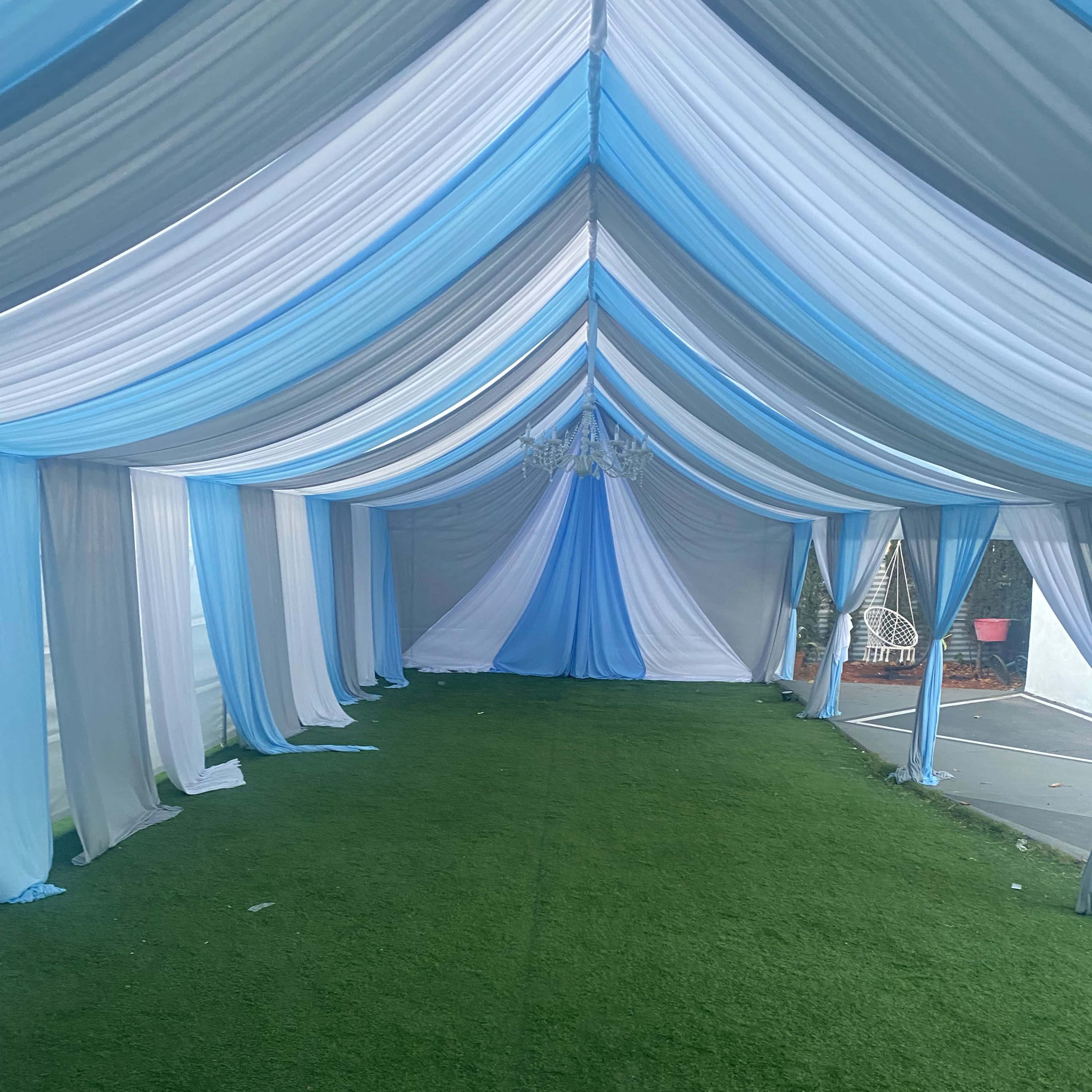 A tent interior with blue and white draped fabric and artificial grass flooring.