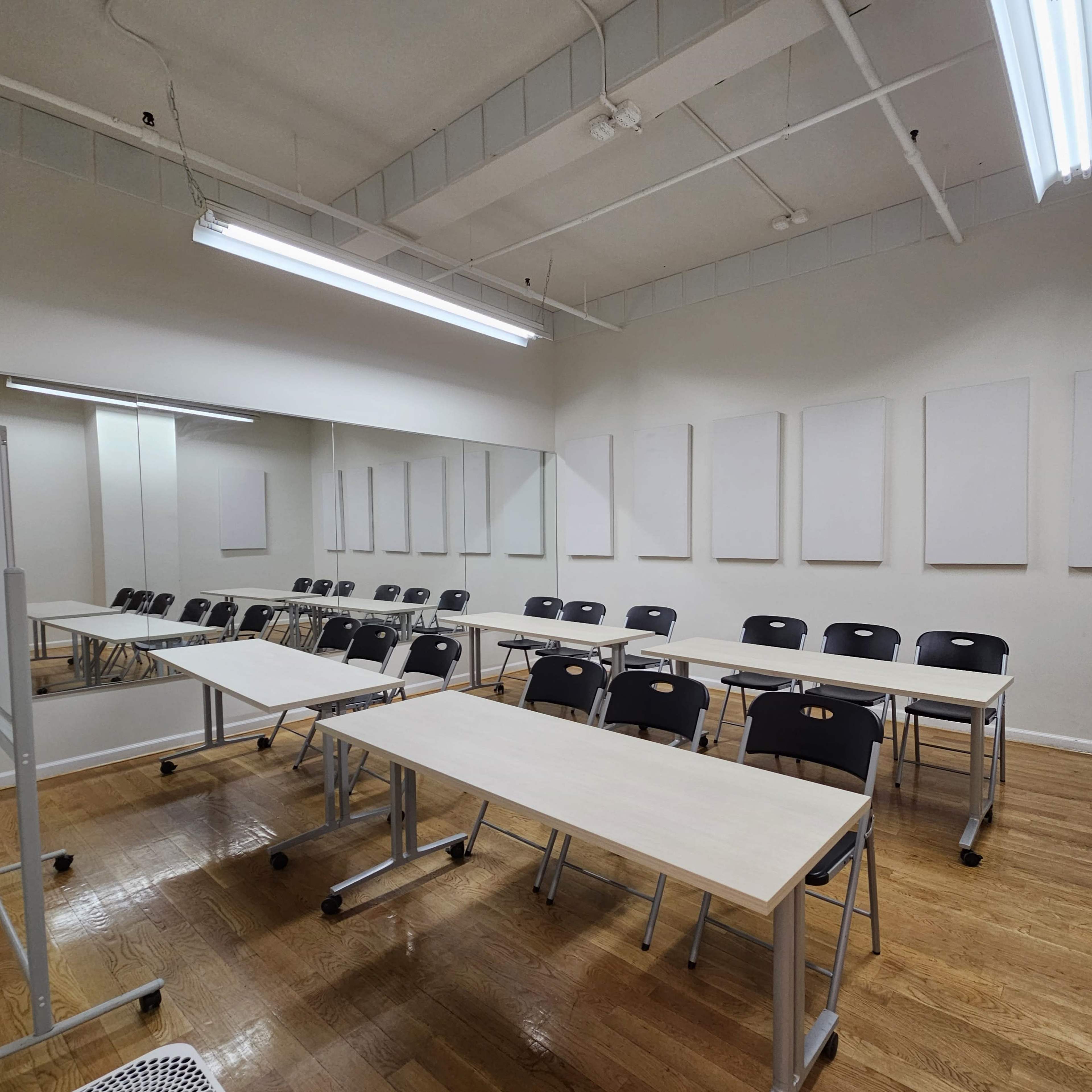 An empty classroom features rows of tables and chairs, with blank wall spaces and overhead lighting.