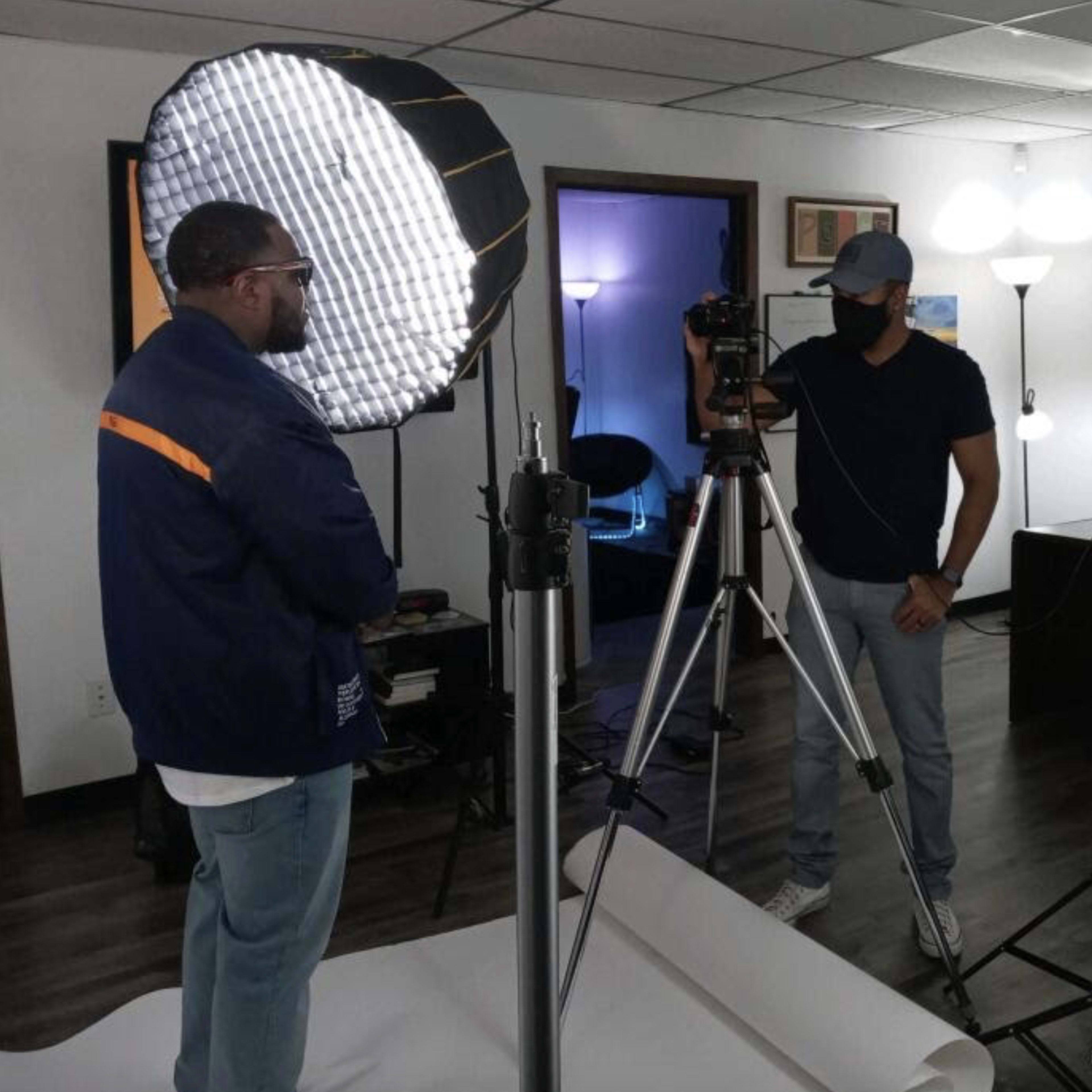 Two individuals are setting up a camera and lighting equipment in an office space for a photo or video shoot.