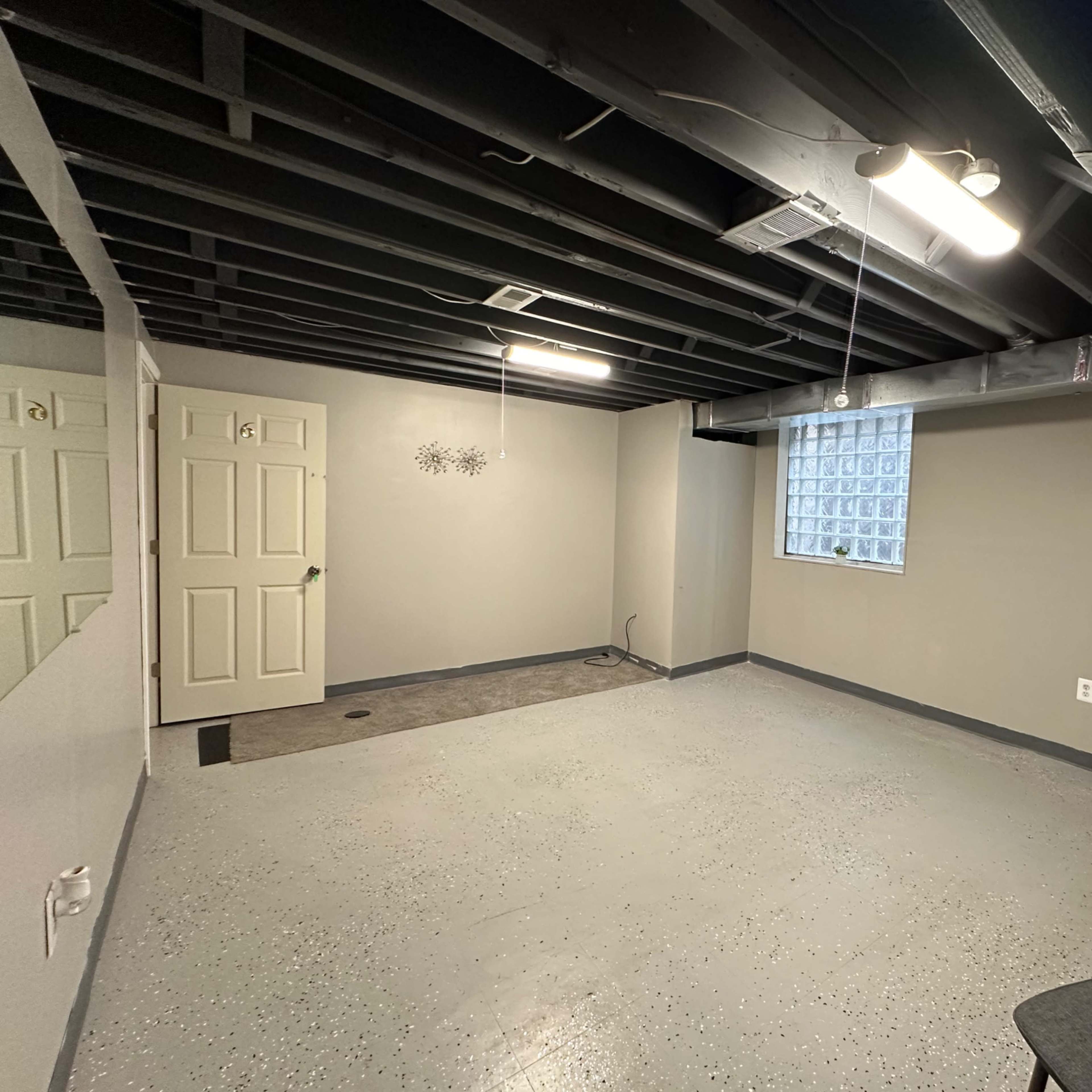 A finished basement with concrete flooring, gray walls, a small window, and two closed doors.