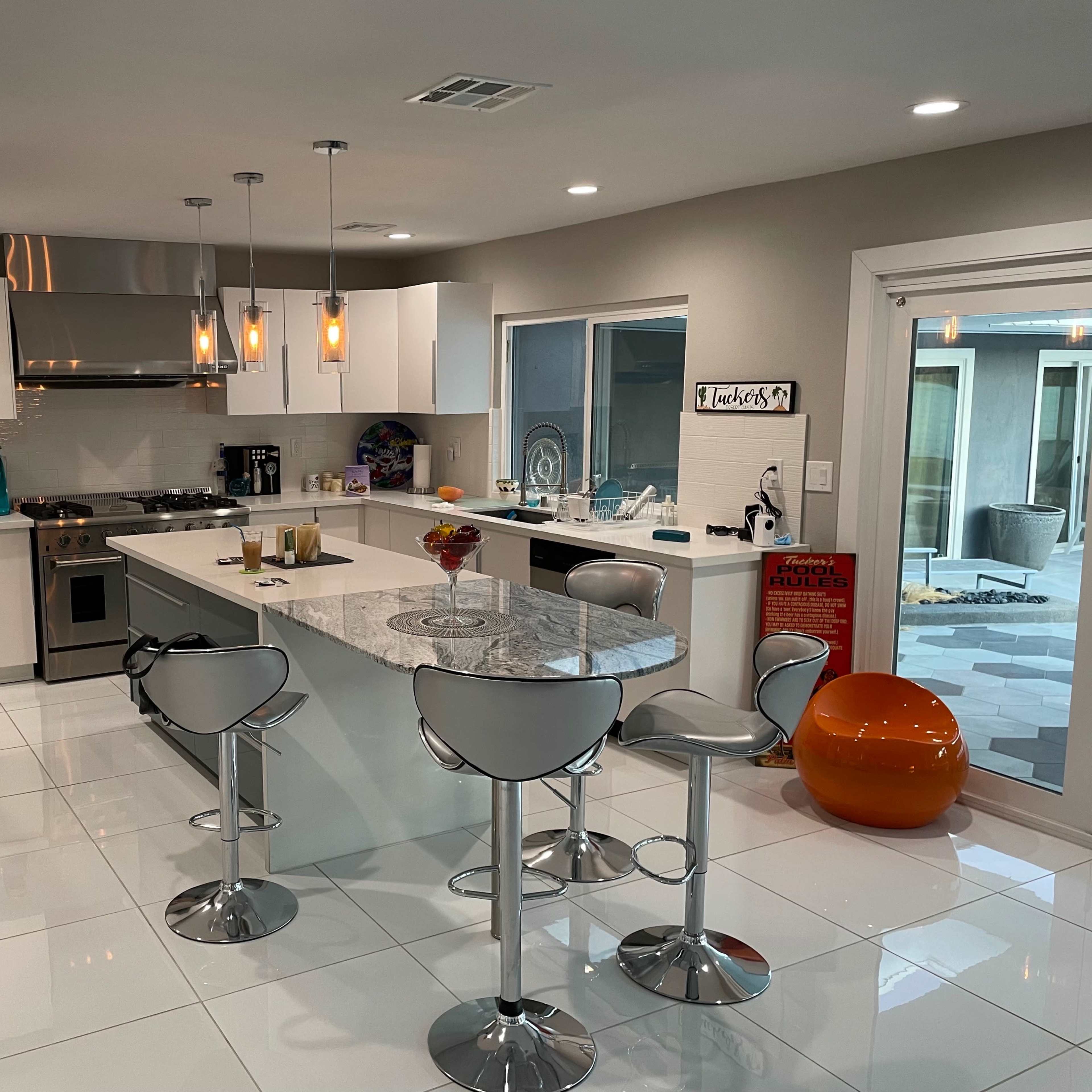 A modern kitchen with a central island featuring bar stools, sleek cabinetry, and appliances, illuminated by pendant lights.