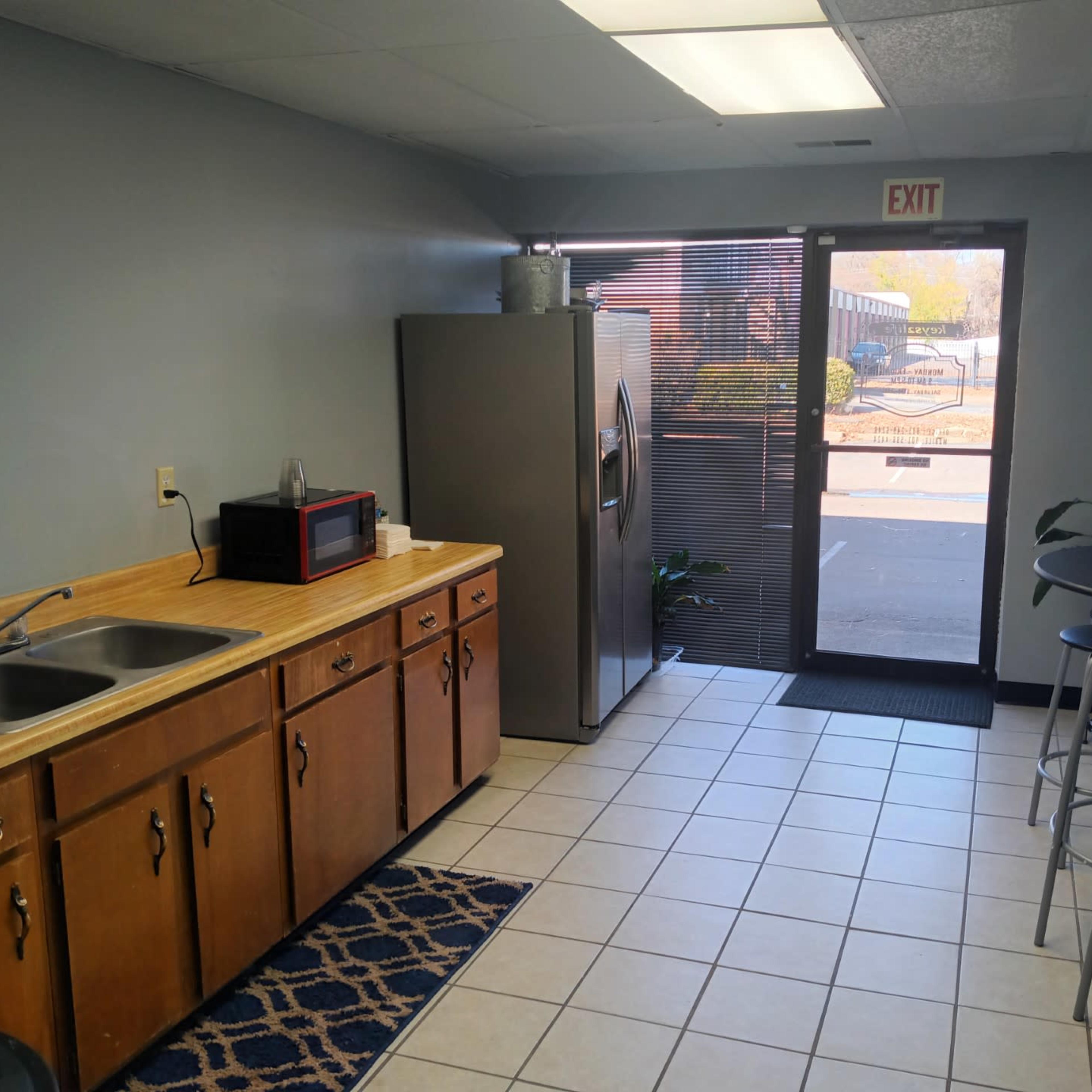 A small kitchen area features a sink, countertop, refrigerator, microwave, and a round table with stools near a glass door that leads outside.
