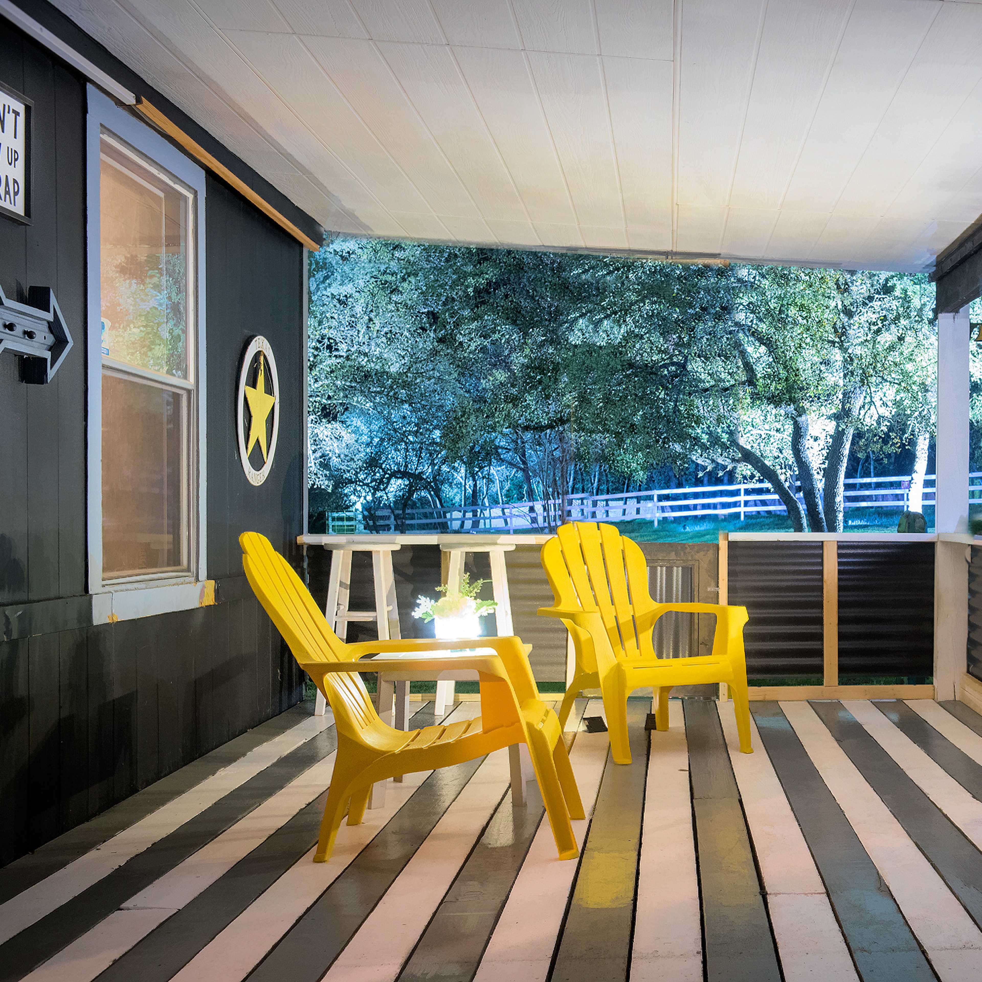 A porch with two yellow chairs, a small table, and illuminated trees in the background.