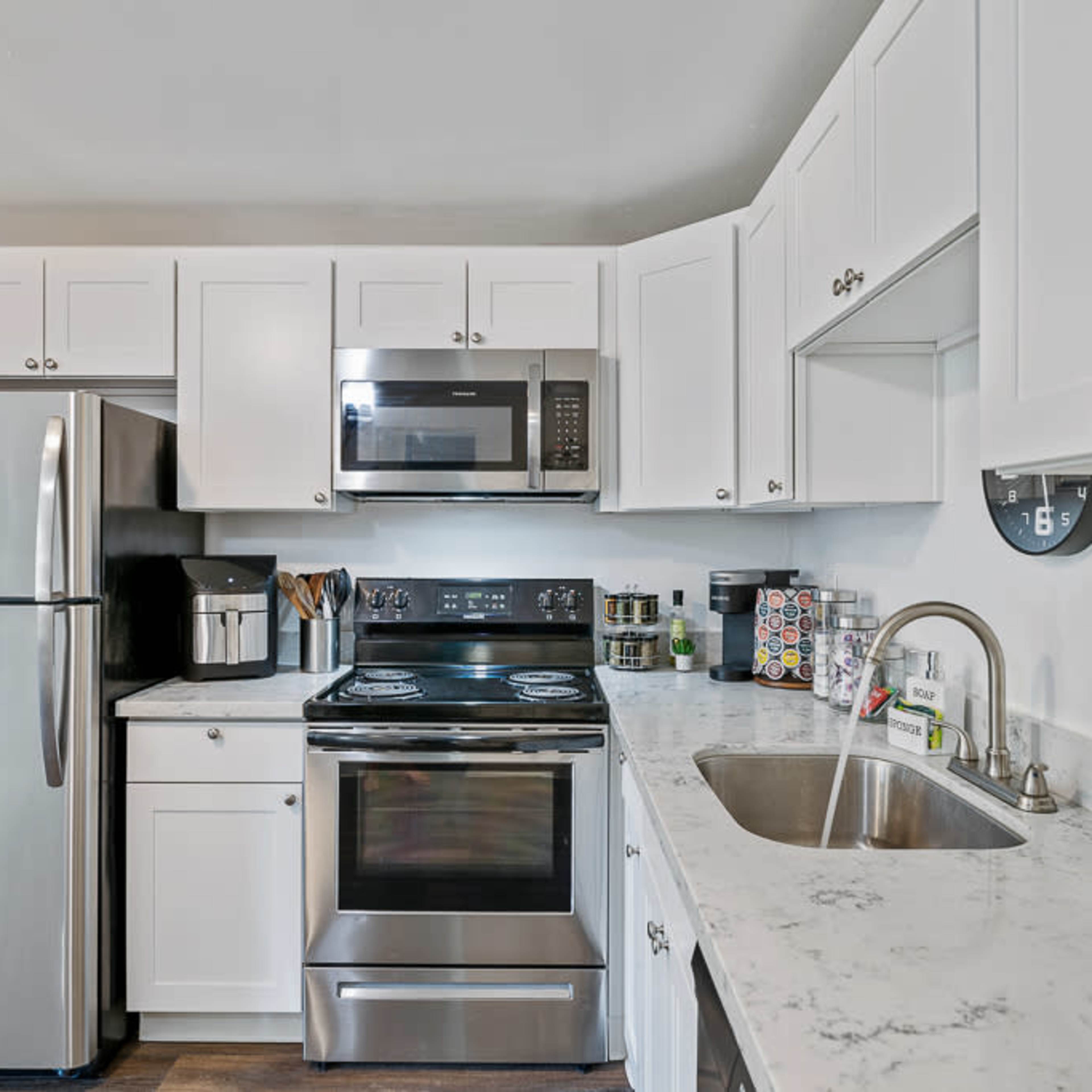 The kitchen features white cabinets, a stainless steel refrigerator, and modern appliances, including a microwave and stove, set against a marble countertop.