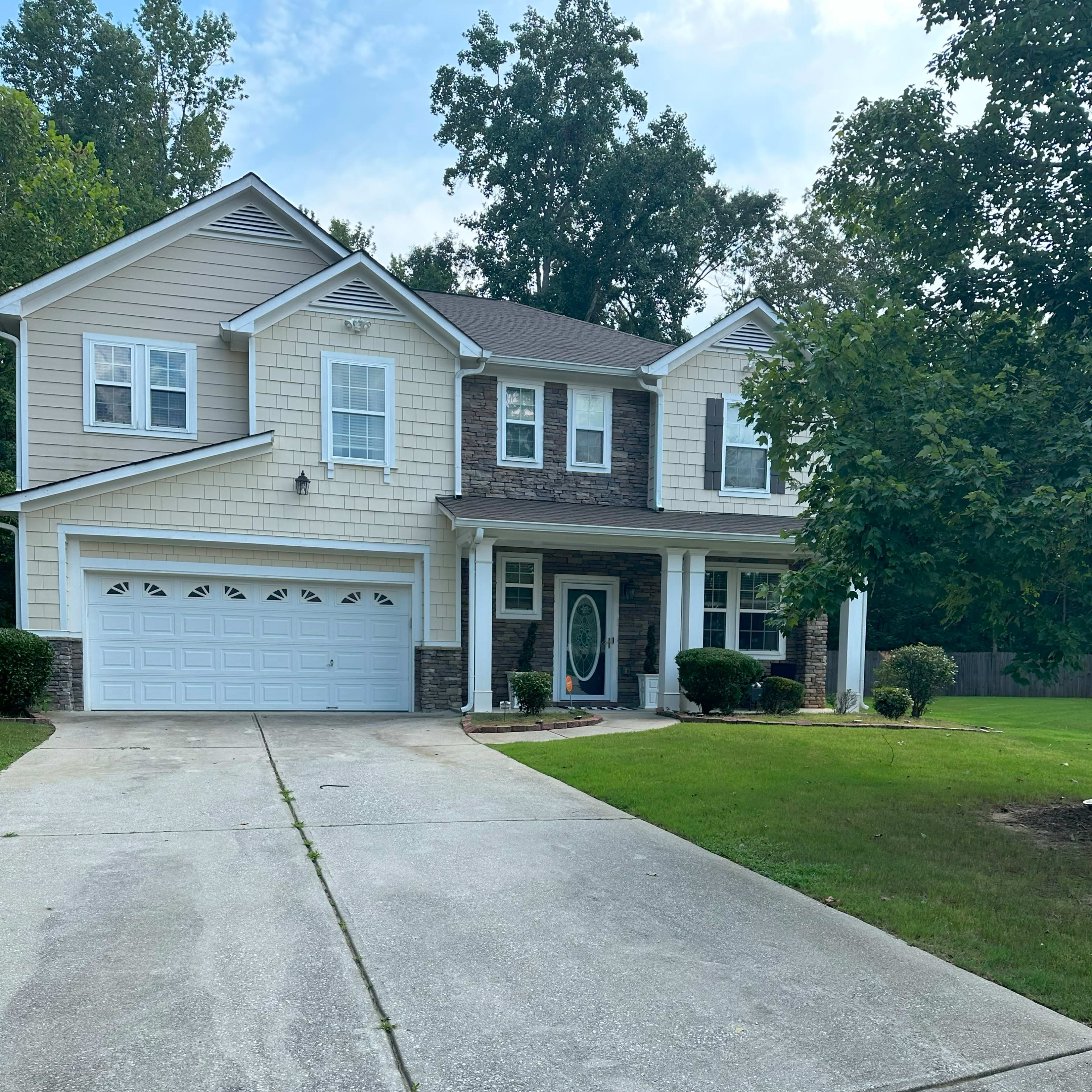 A two-story house with a stone and siding exterior, a front porch, and a driveway lined with grass.