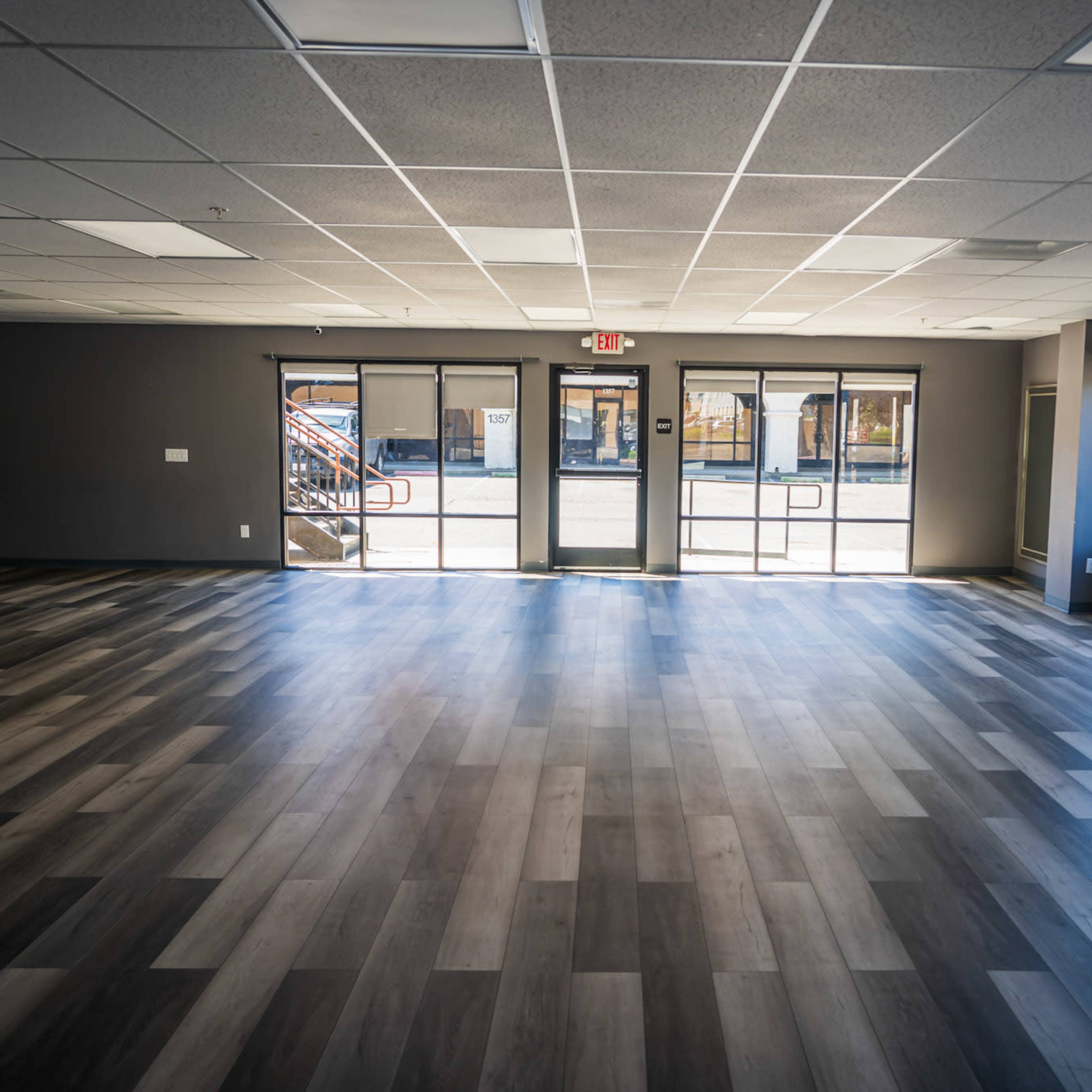 A spacious indoor area with large windows and a wooden floor, allowing natural light to enter.