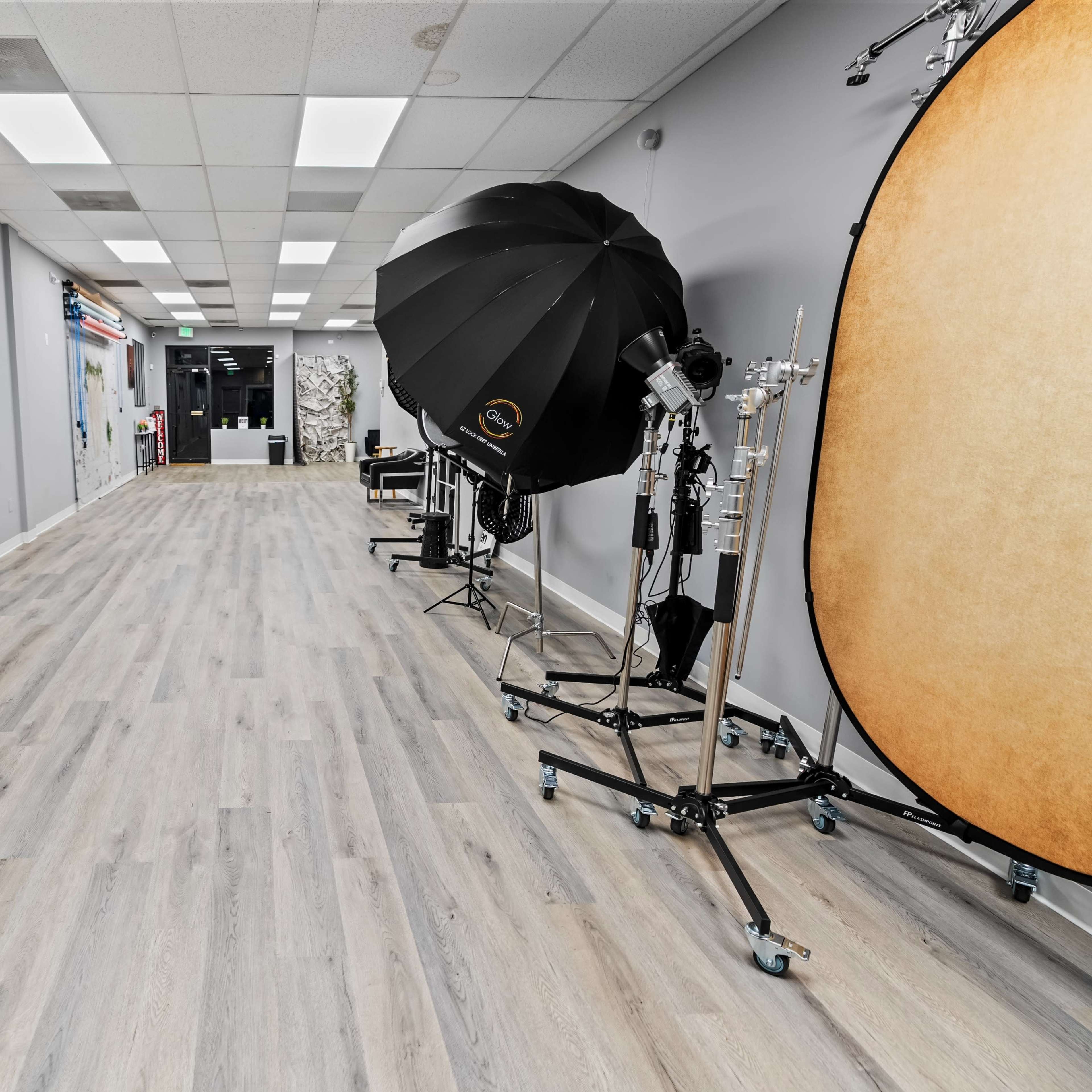 A photography studio with a long hardwood floor, backdrop rolls, and lighting equipment along the walls.