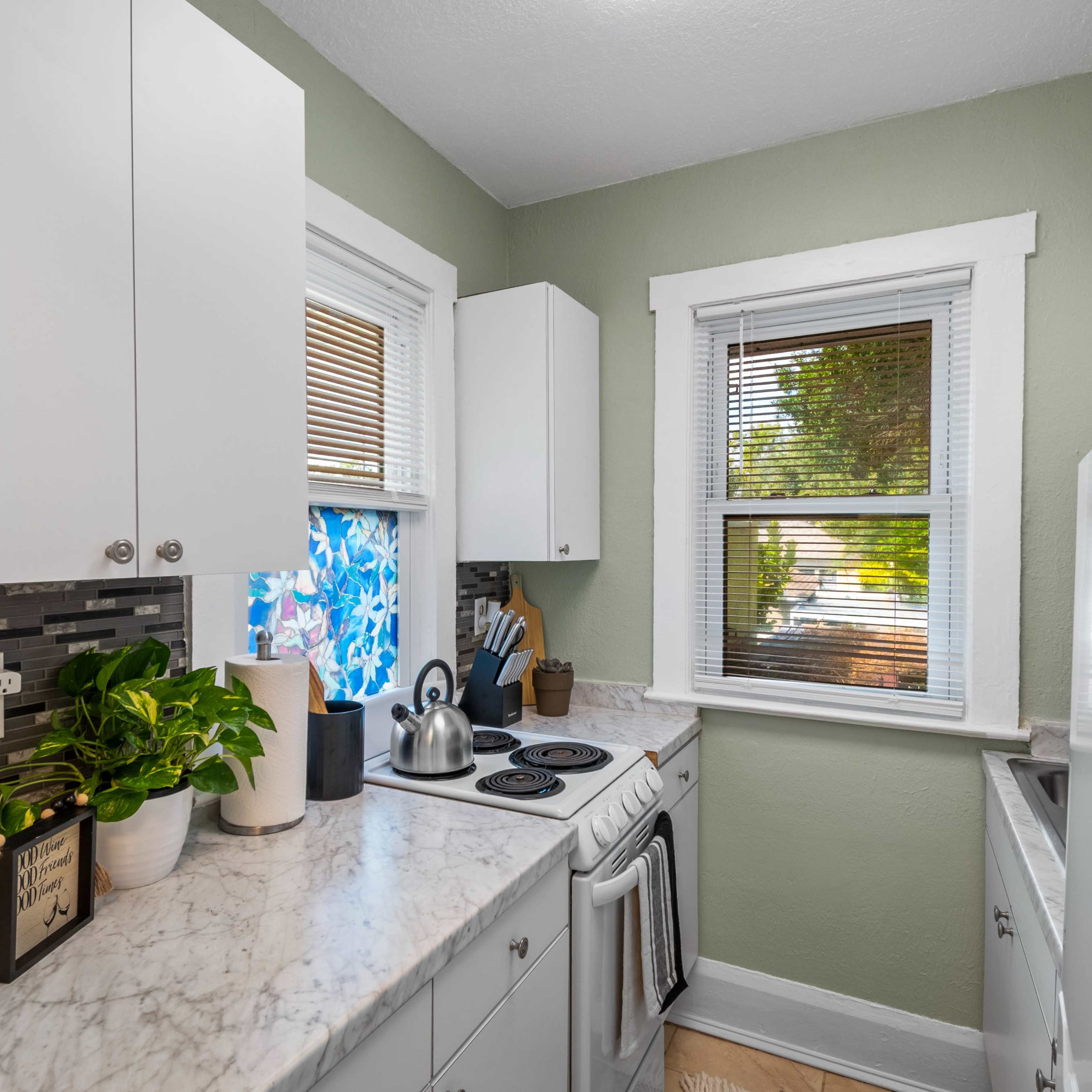 A small kitchen with light green walls, white cabinets, and a marble countertop featuring a stove and a white refrigerator.