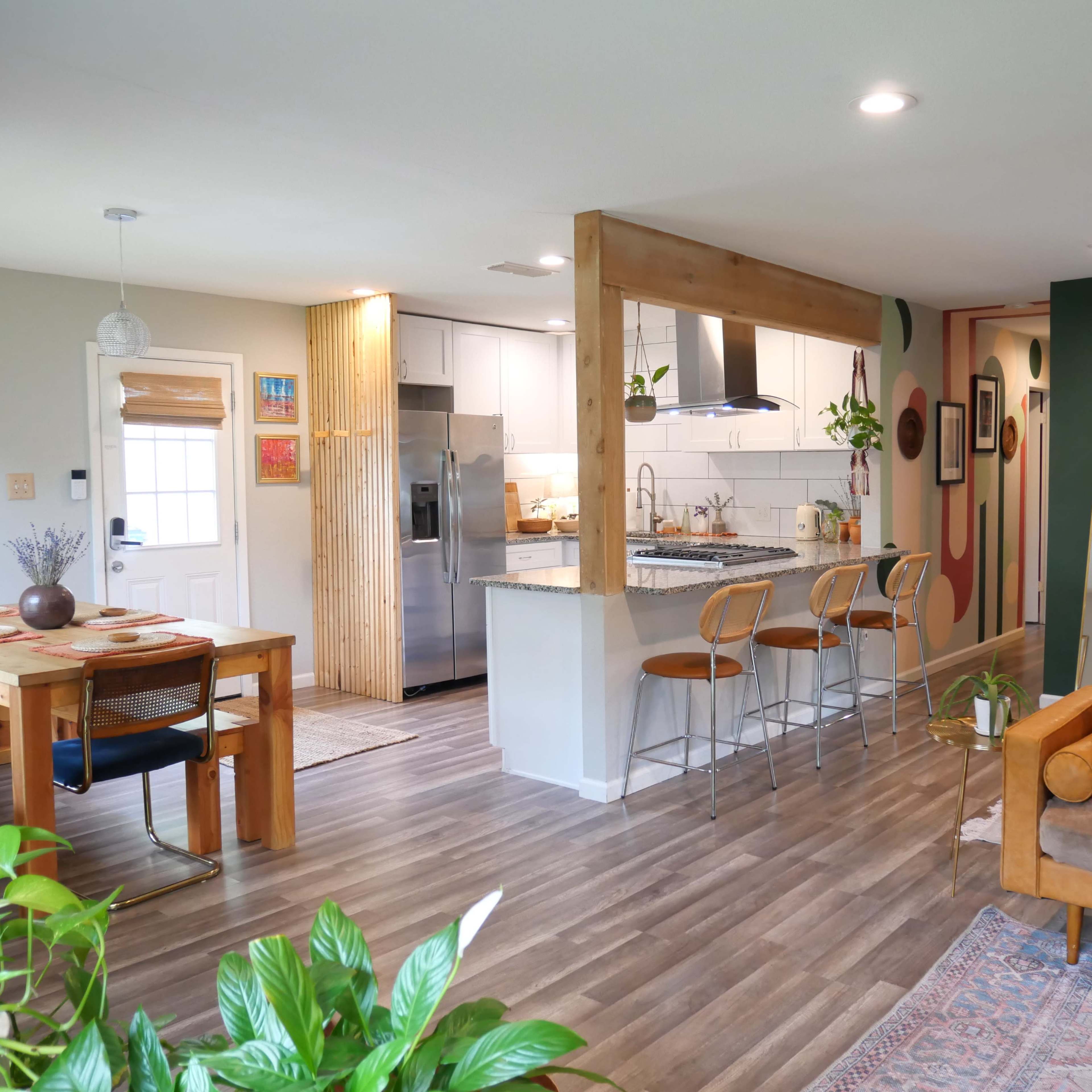 A modern open-concept living space featuring a dining area with a wood table, a kitchen with bar seating, and a cozy seating area with a sofa.