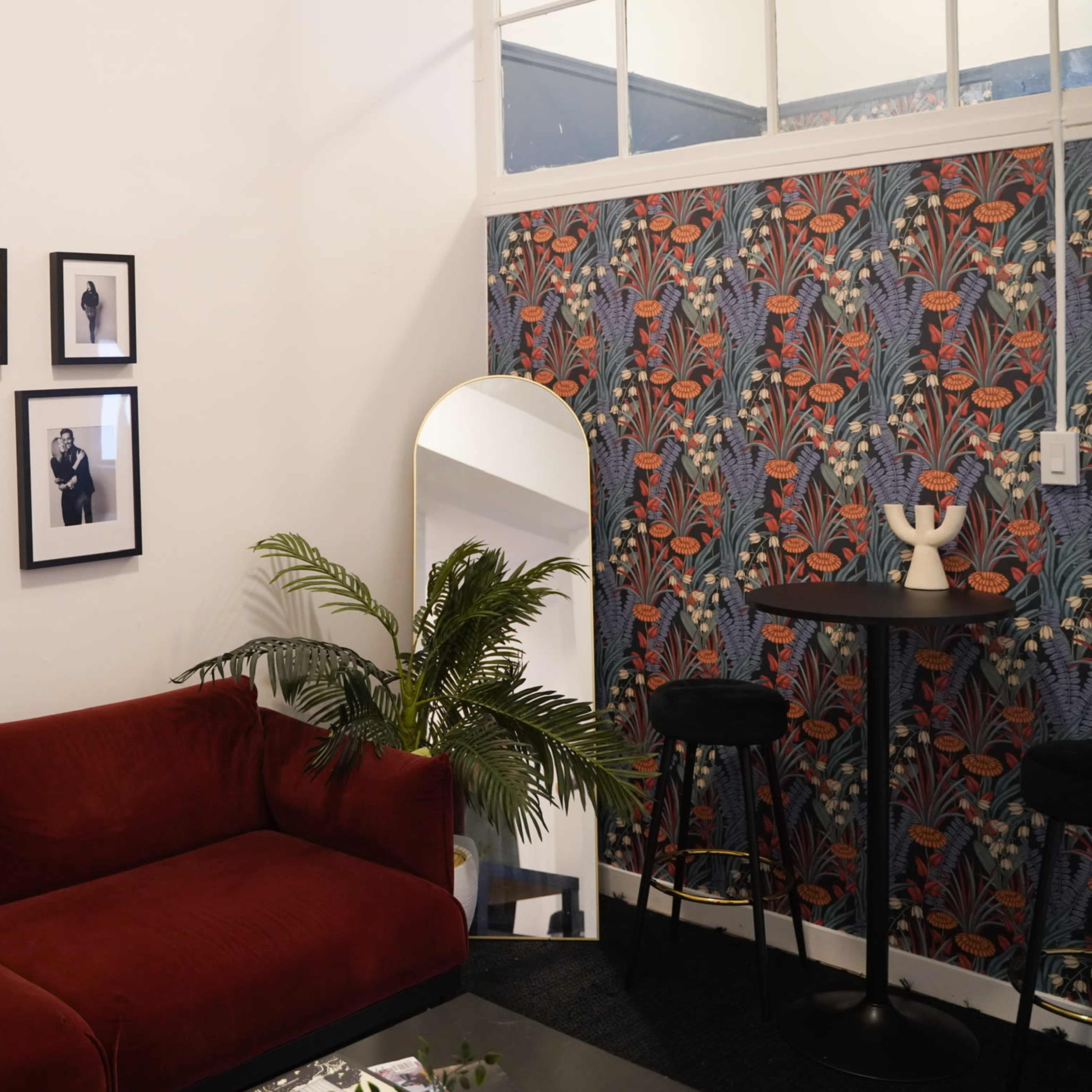A living room with a red sofa, a patterned wallpaper on one side, and framed black-and-white photographs on the wall.