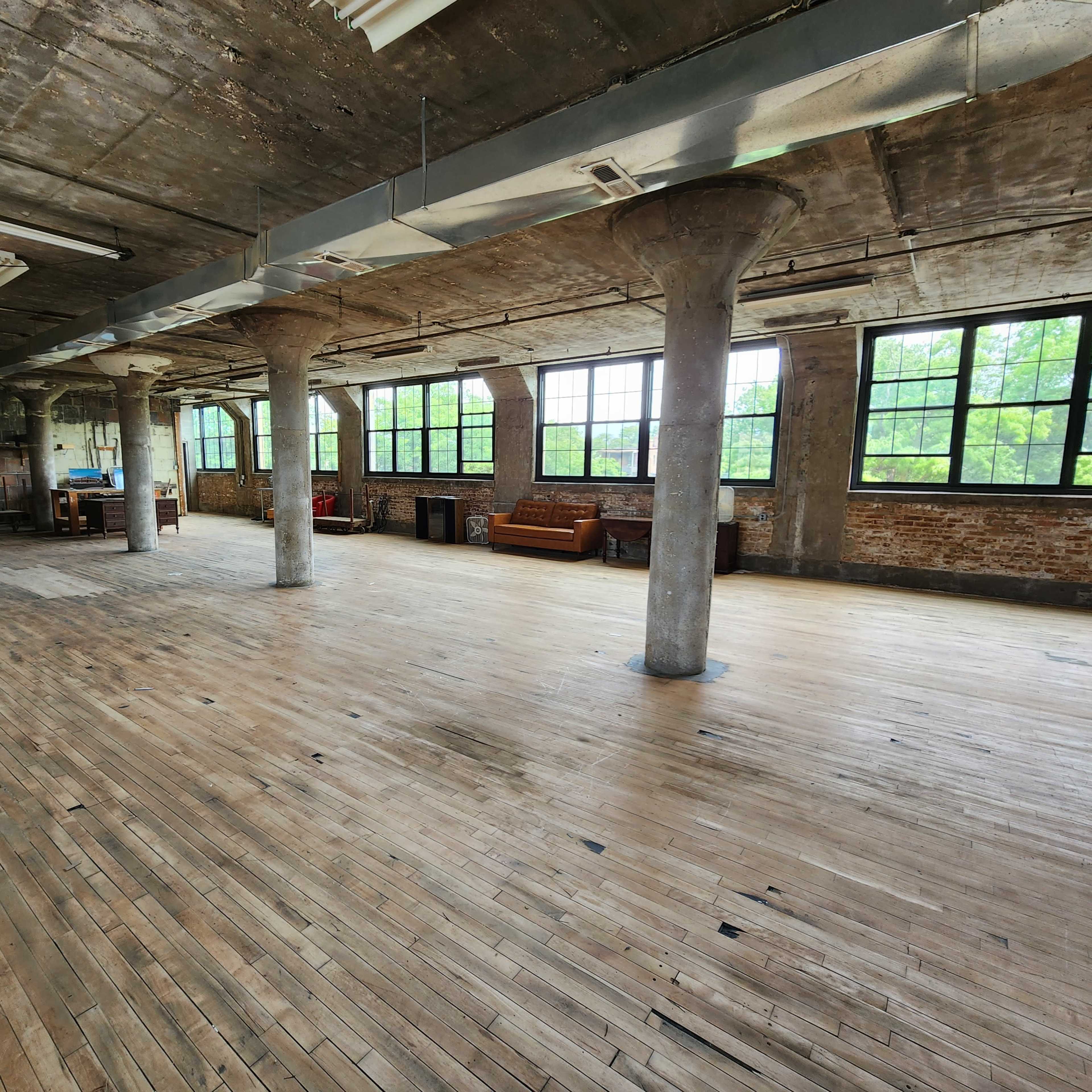 An empty industrial space with wooden floors, large windows, and concrete pillars.
