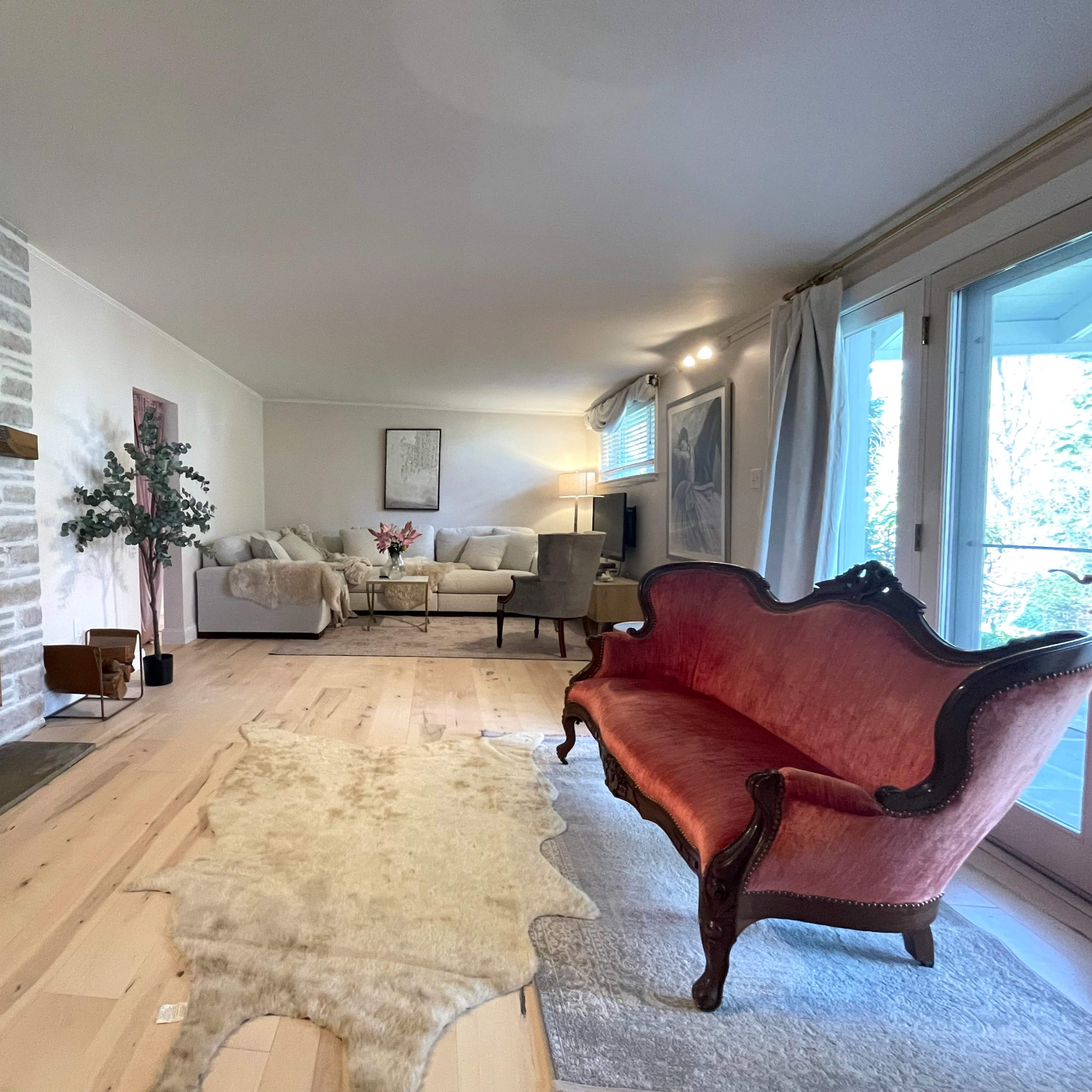 A spacious living room featuring a stone fireplace, a red upholstered loveseat, and a seating area with two light-colored couches and a coffee table.