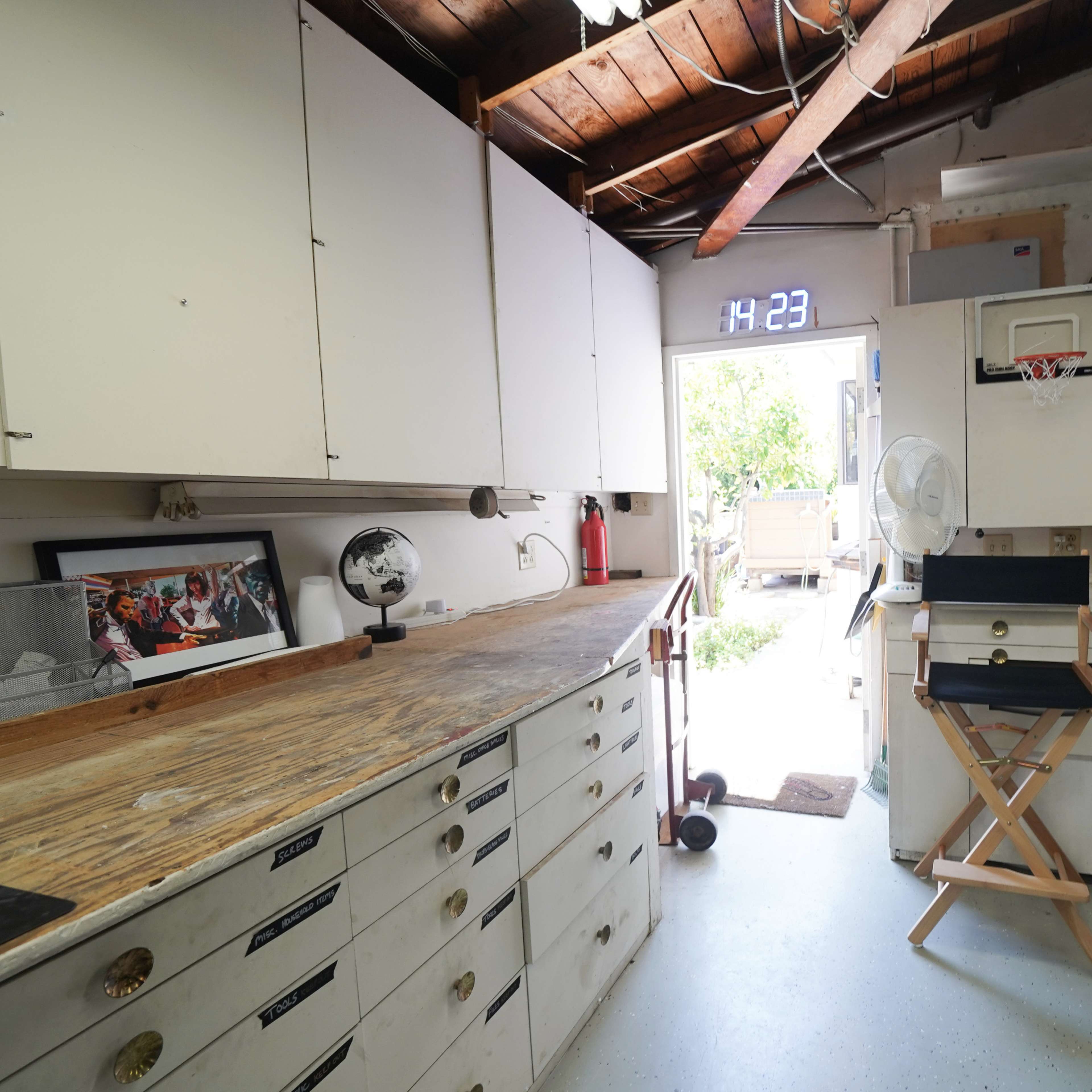 A well-organized workshop or garage space with wooden counters, cabinetry, and a doorway leading to an outdoor area.