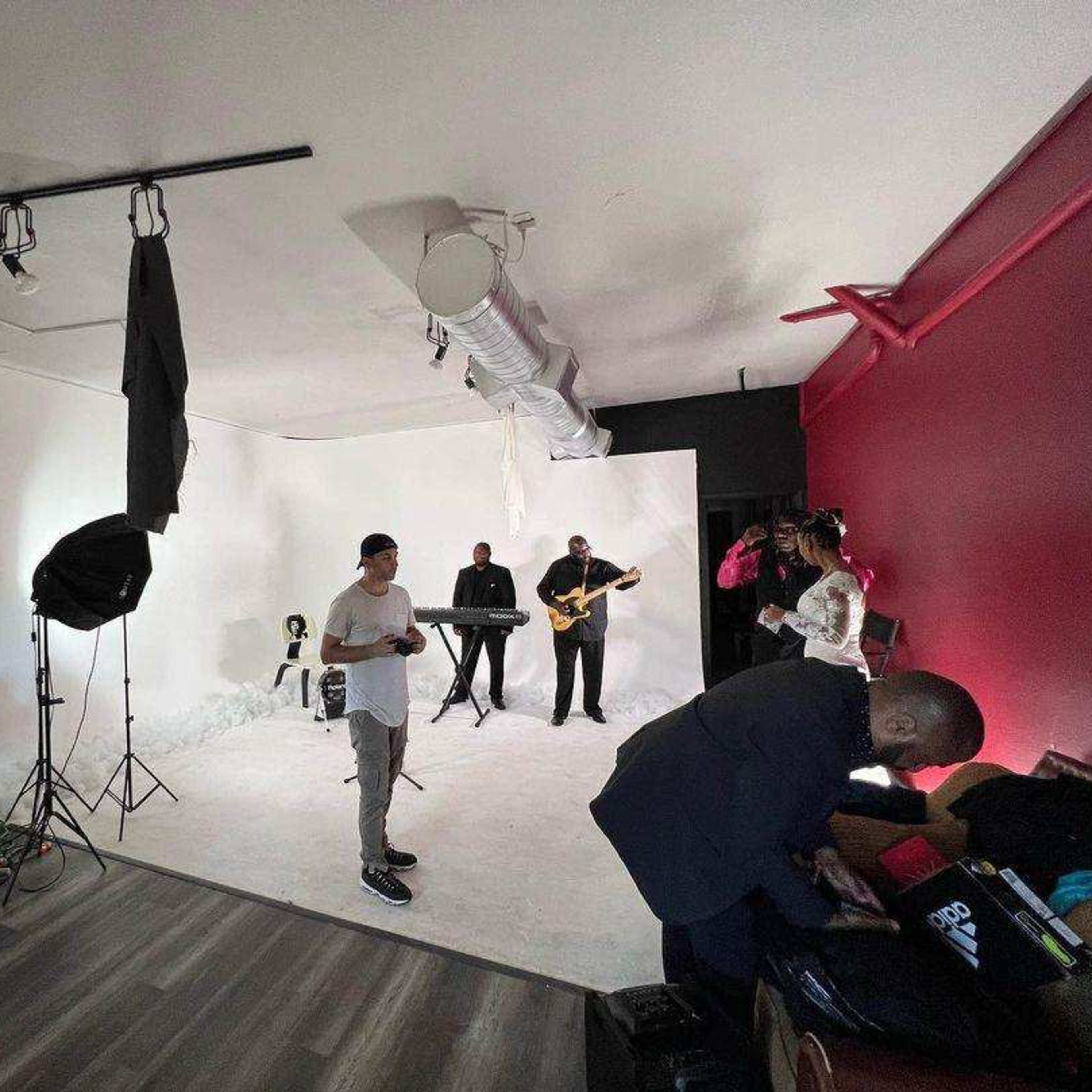 A music group is performing in a studio with a white backdrop and various equipment set up around them.