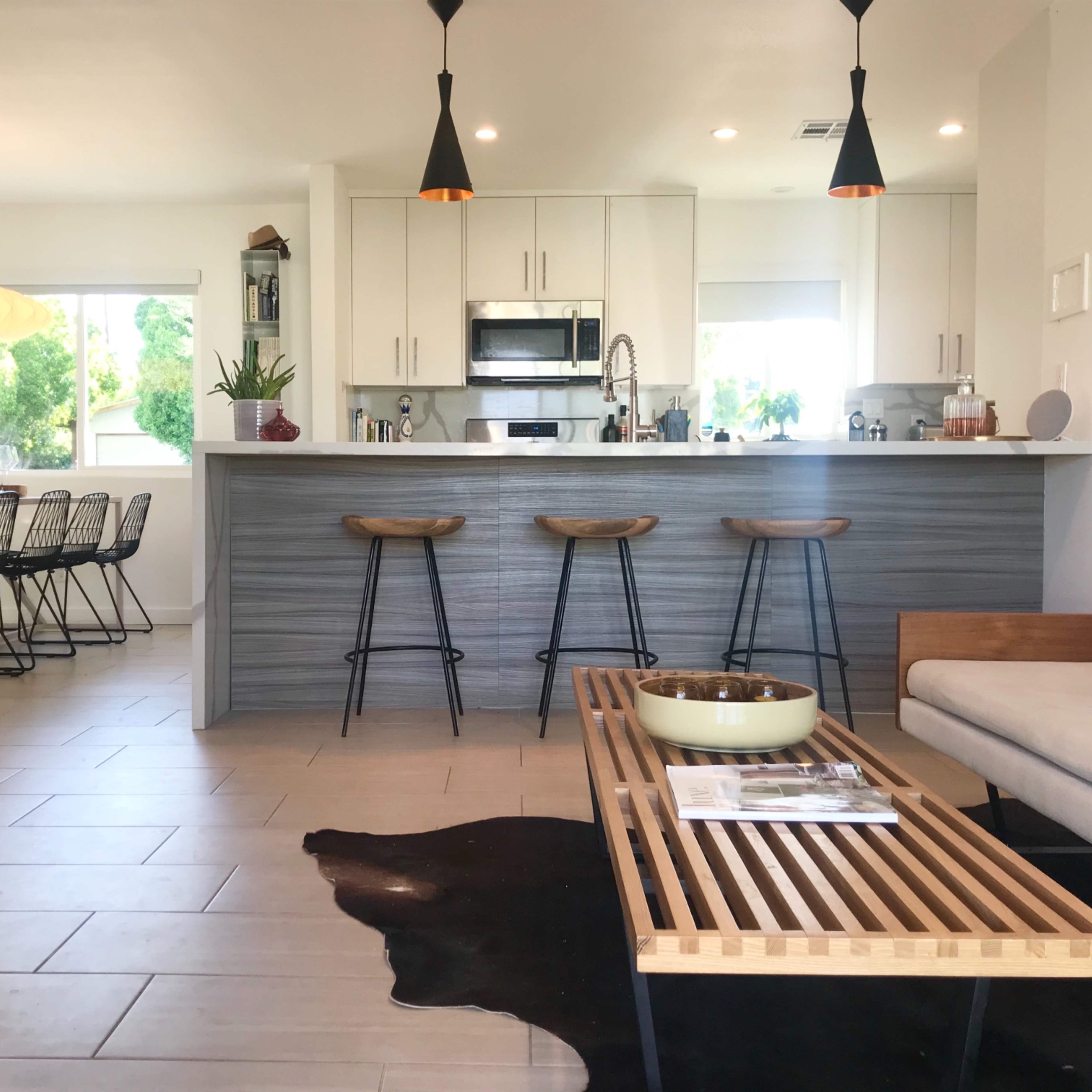 A modern open-concept living space featuring a kitchen with bar stools, a dining area with a table, and a seating area with a couch and coffee table.