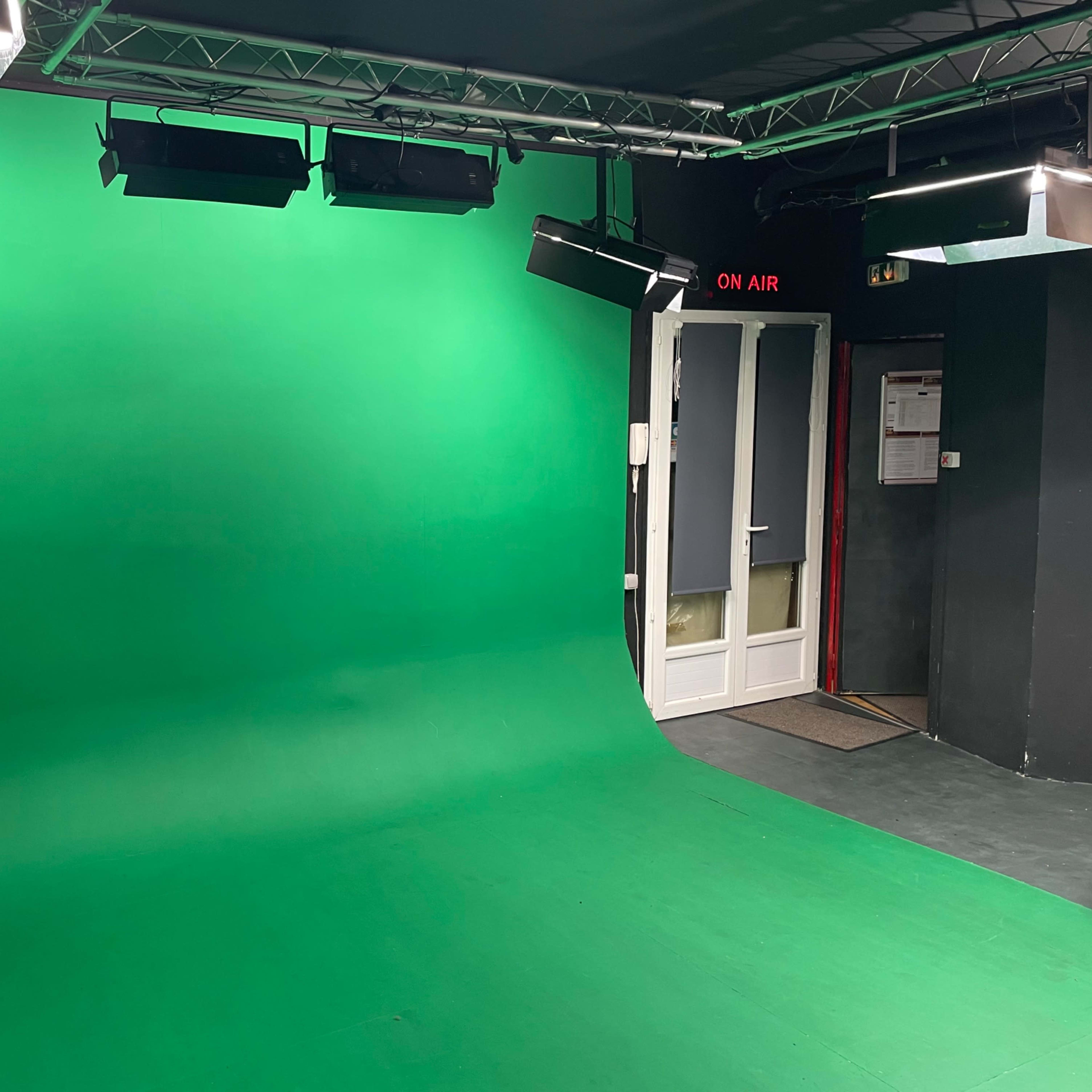 A green screen studio with a seamless green backdrop, overhead lights, and a door labeled "ON AIR."