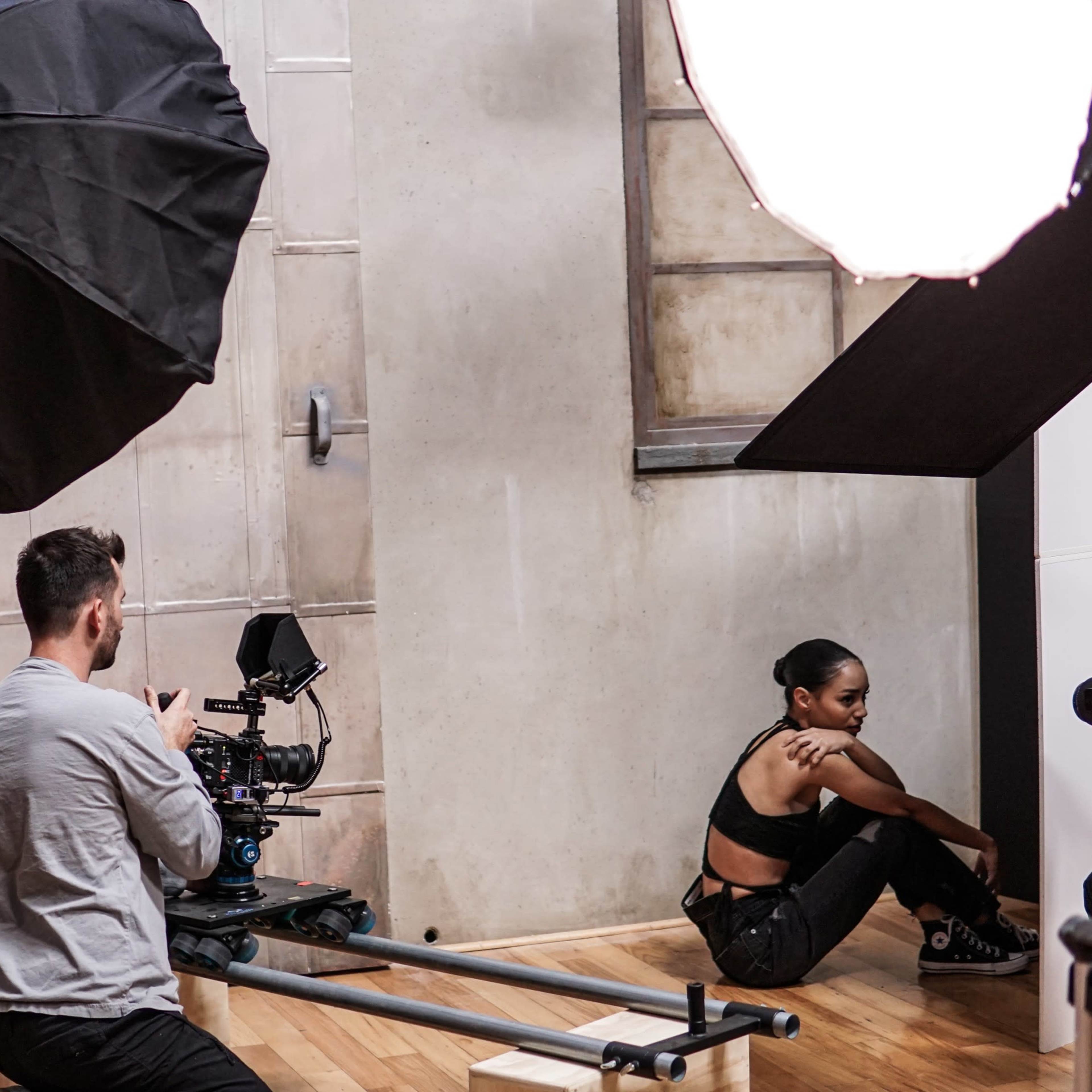 A photographer captures a model posing in a studio setting with large softbox lights and a camera on a slider track.