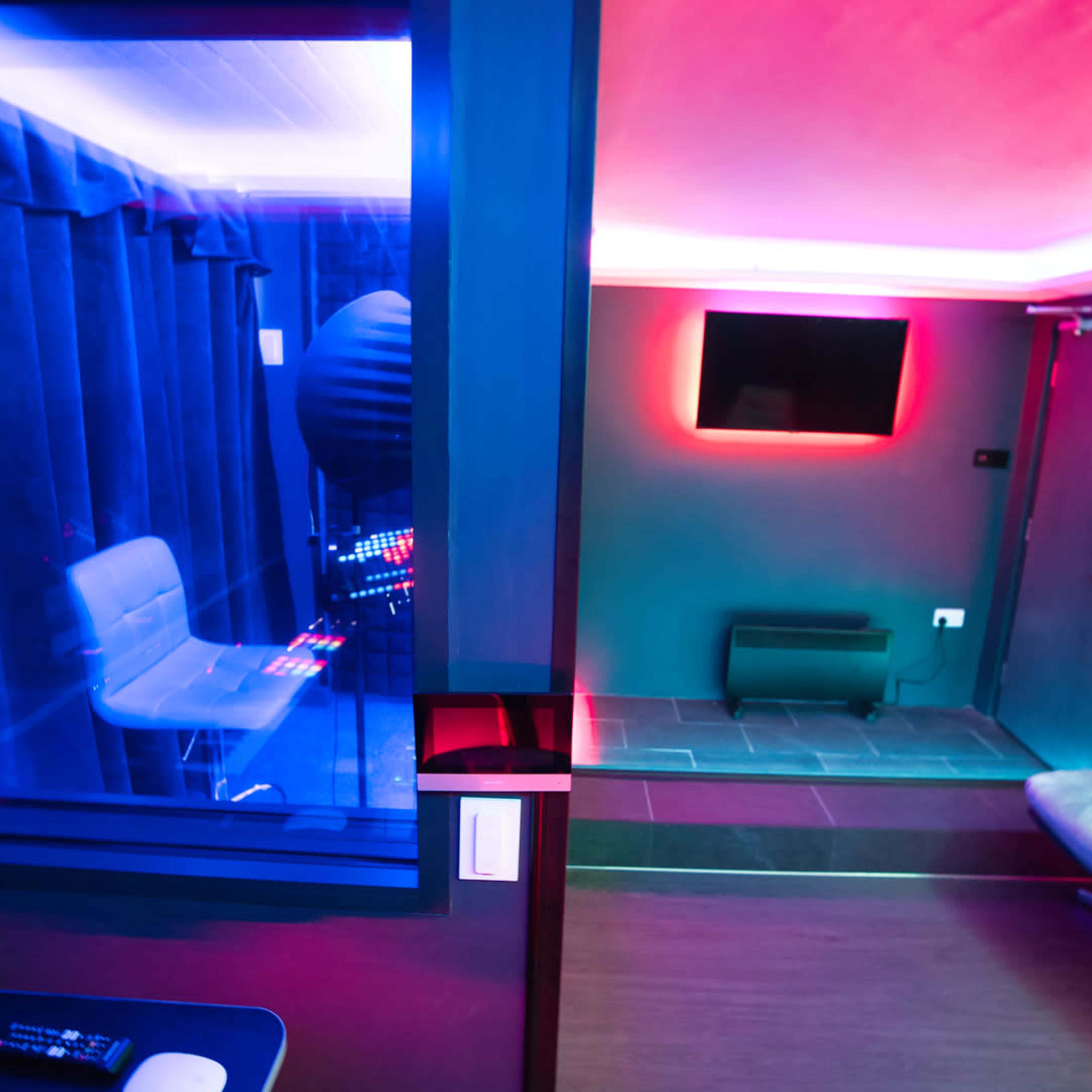 A modern recording studio with a control area on the left, a vocal isolation booth visible through a glass wall, and a softly lit lounge area on the right.