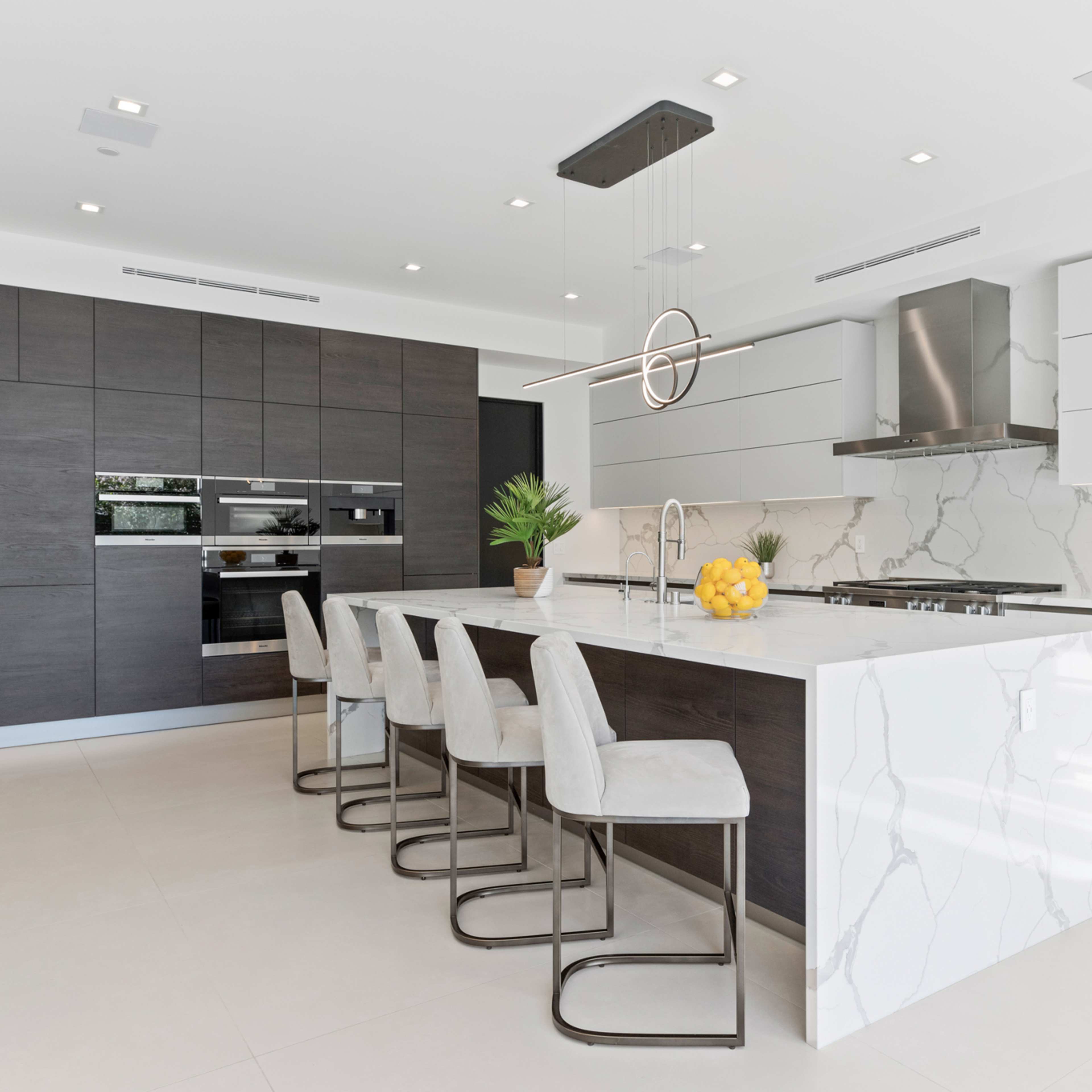 A modern kitchen featuring dark cabinetry, white countertops with marble veining, and a central island with four bar stools.