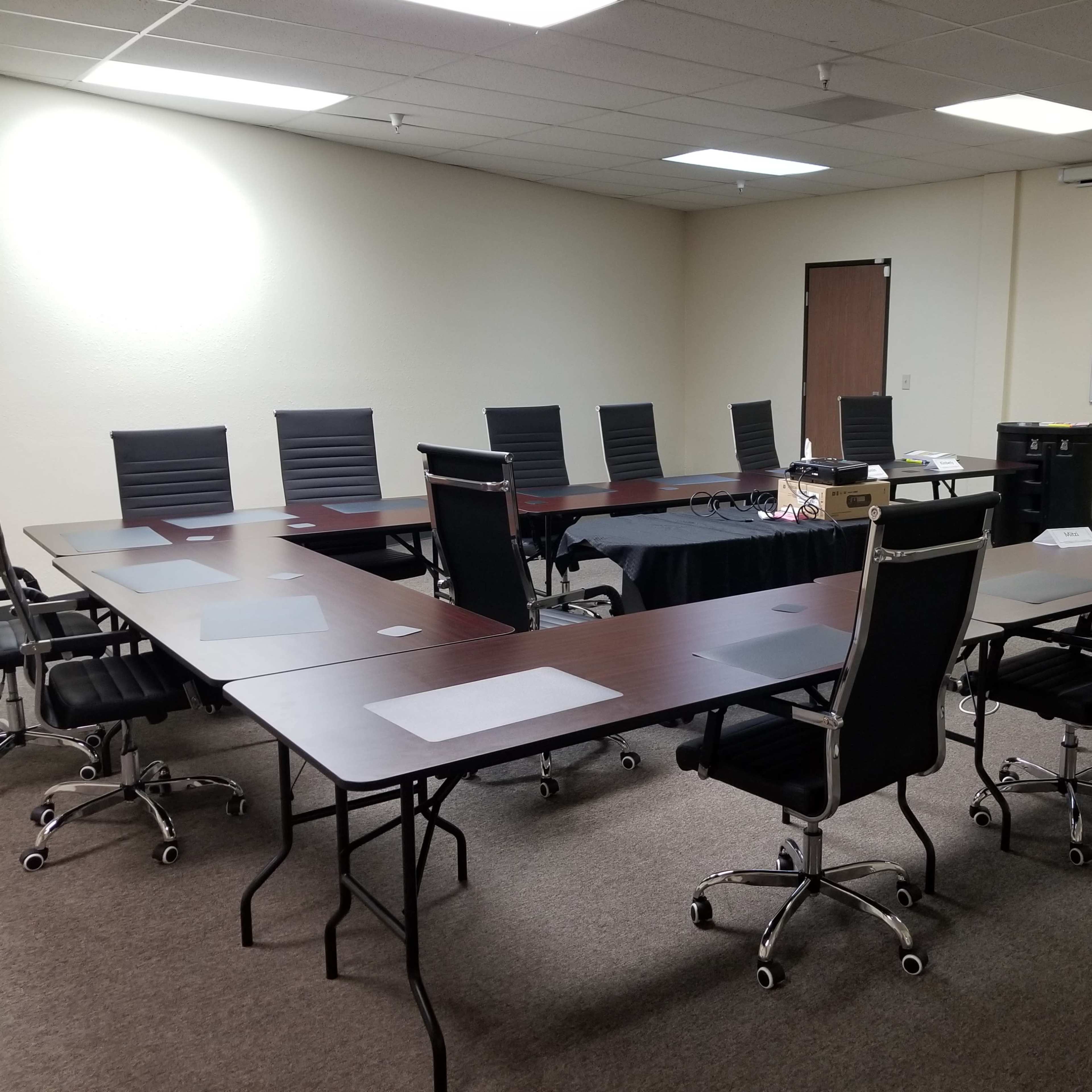 A conference room with a large oval table surrounded by several black office chairs and a whiteboard covered in notes on the wall.