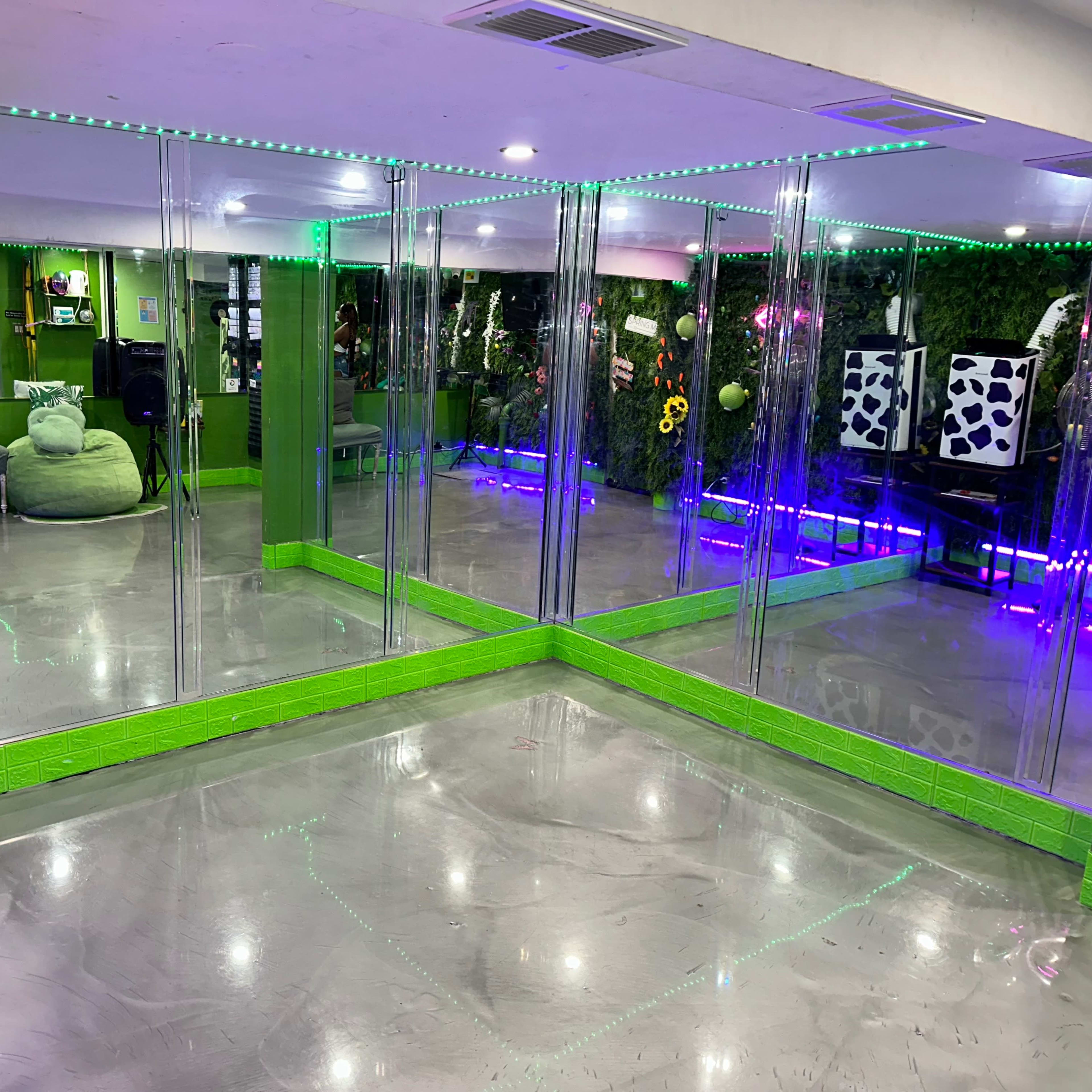 A room with mirrored walls, green accents, and colorful lighting, featuring seating areas and indoor plants.