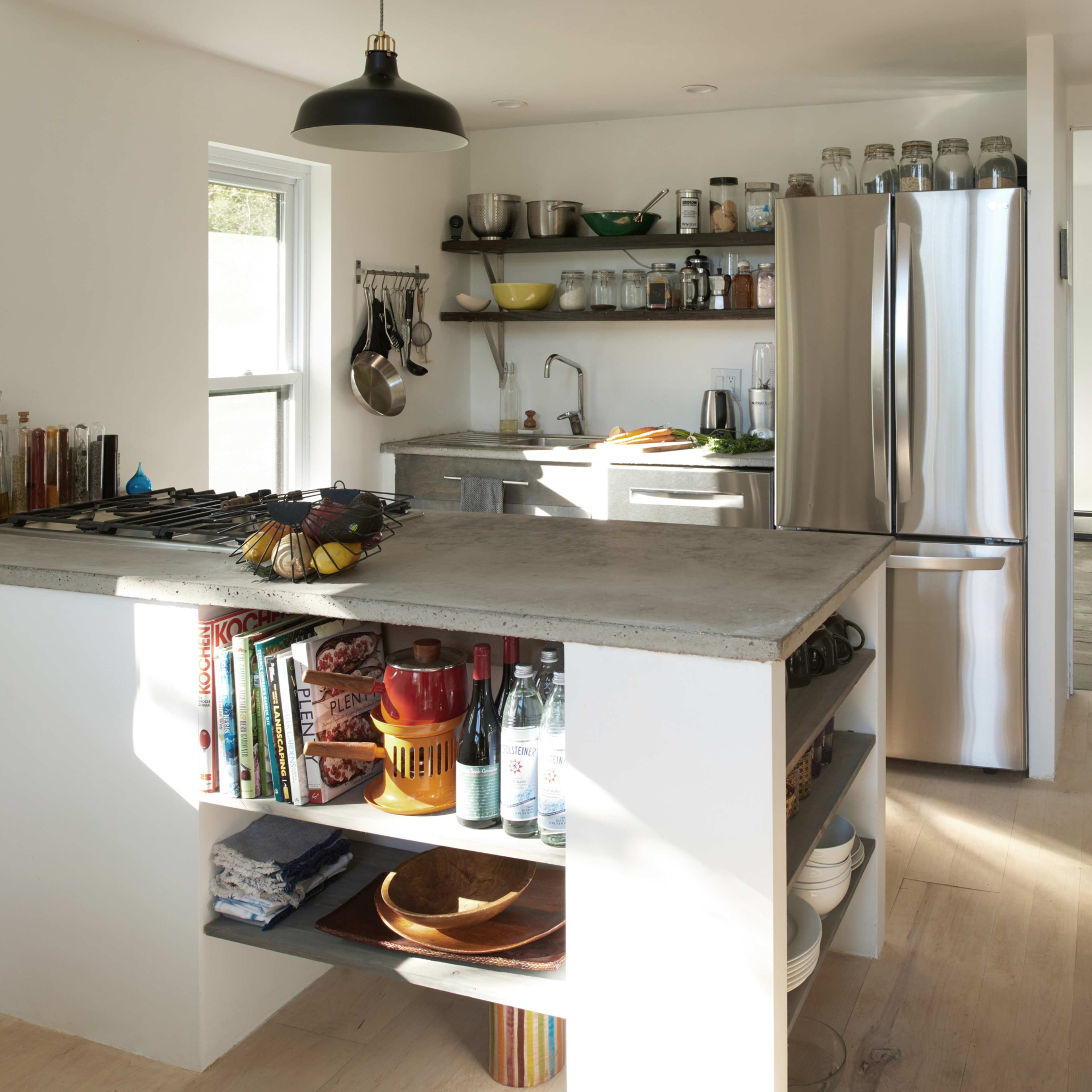 A modern kitchen with a concrete island, stainless steel appliances, and open shelving displaying various kitchen items.